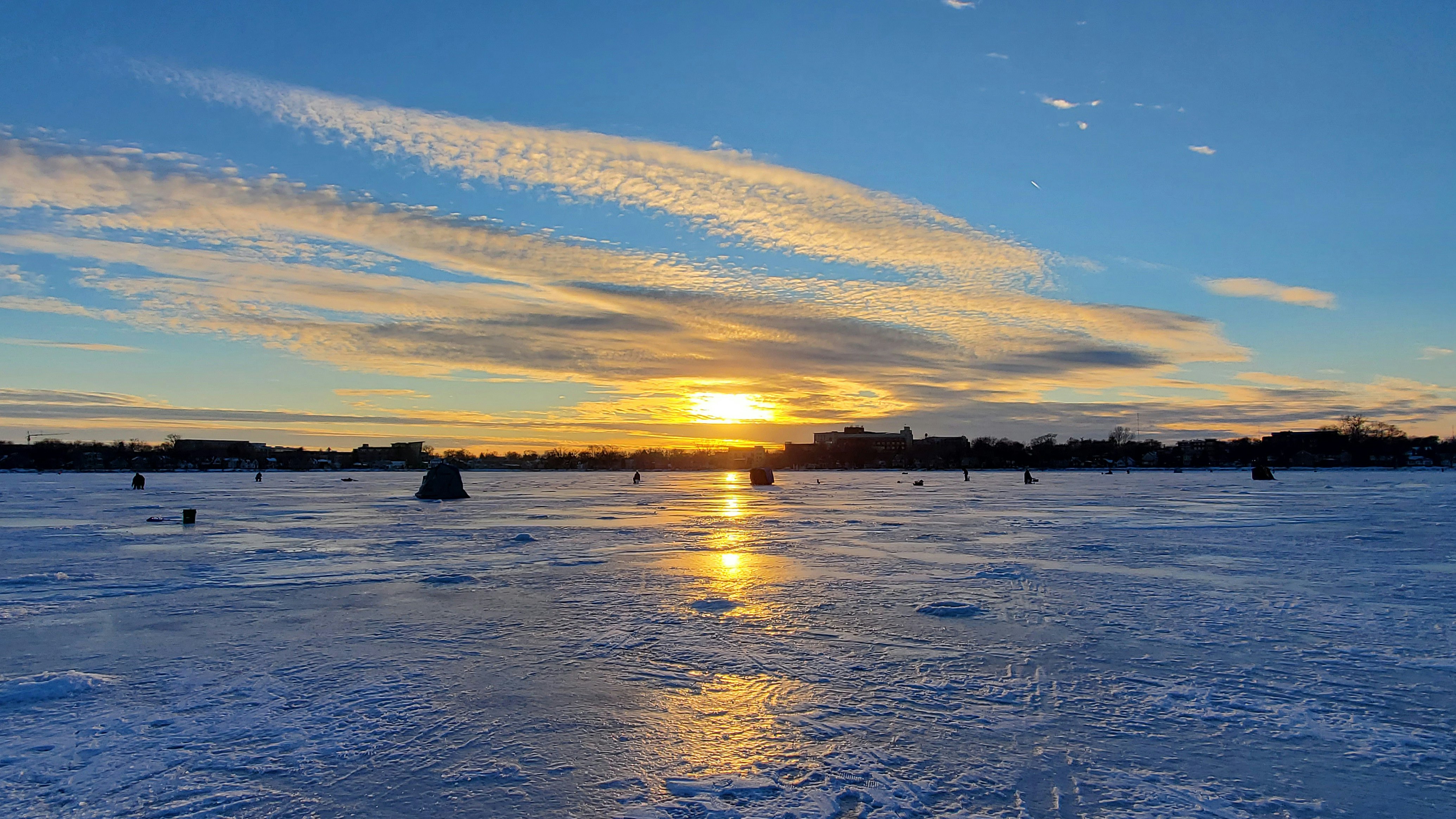 People ice fishing at sunset on a frozen lake