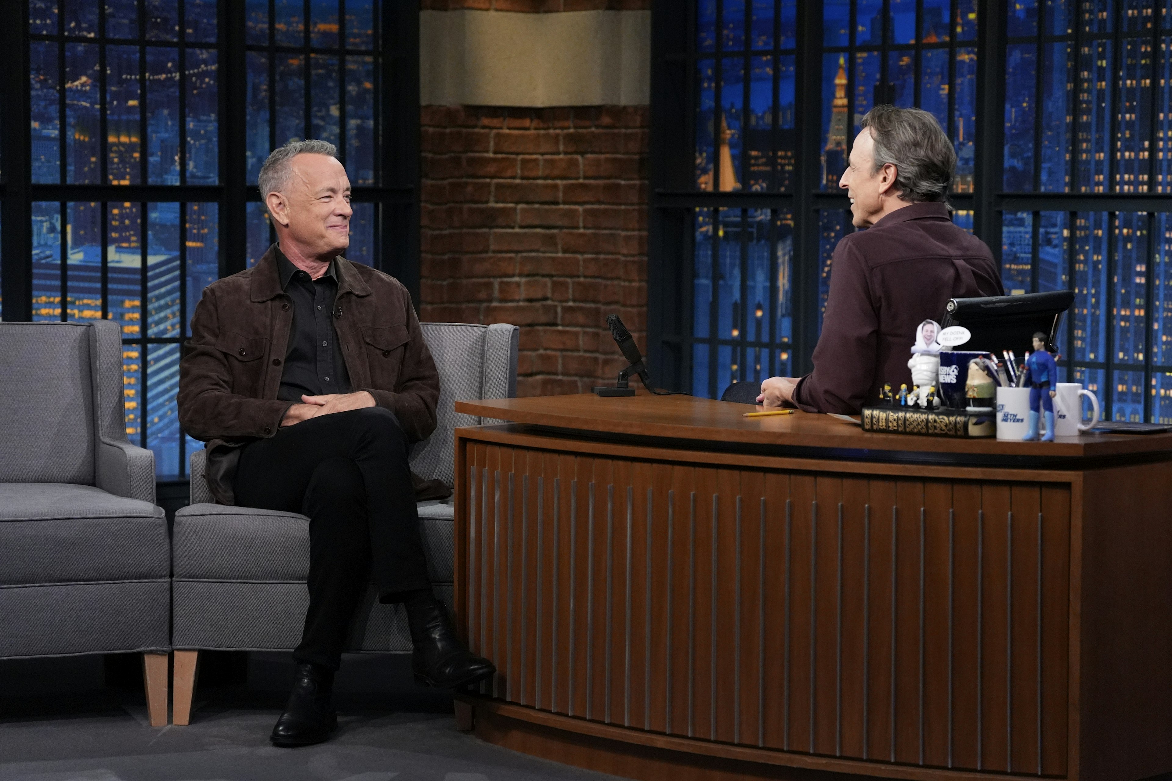 Two men sit in a TV studio in discussion. One is famous actor Tom Hanks, the other is the host, Seth Meyers