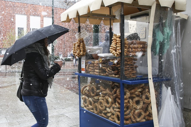 A woman with an umbrella buys a traditional obwarzanek (pretzel) from a stall during heavy snow in spring time in Kraków, Poland