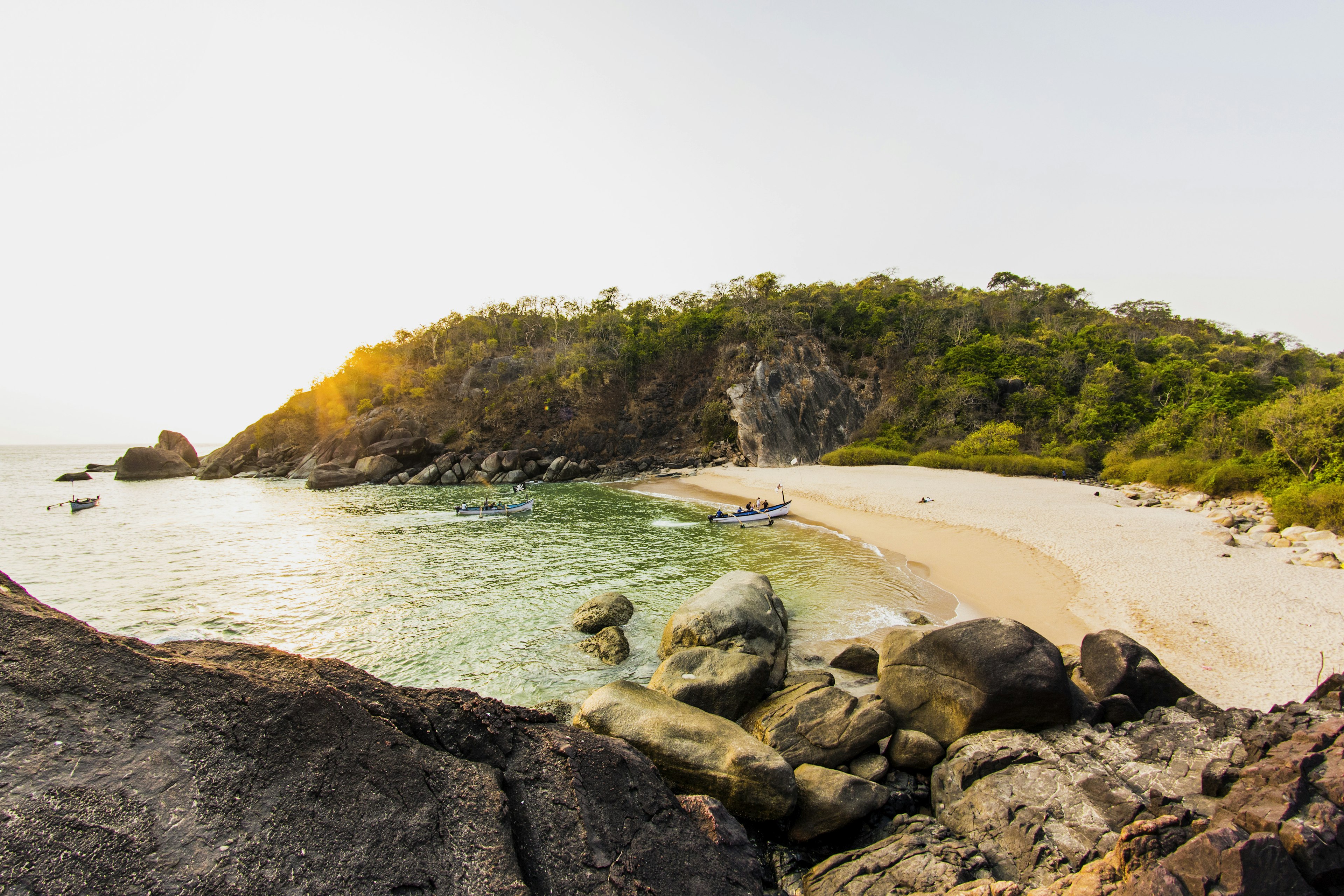 Butterfly Island: a crescent of beach with a single canoe moored on the sand, two more canoes are in the sea approaching the beach. Behind the beach is dense jungle.