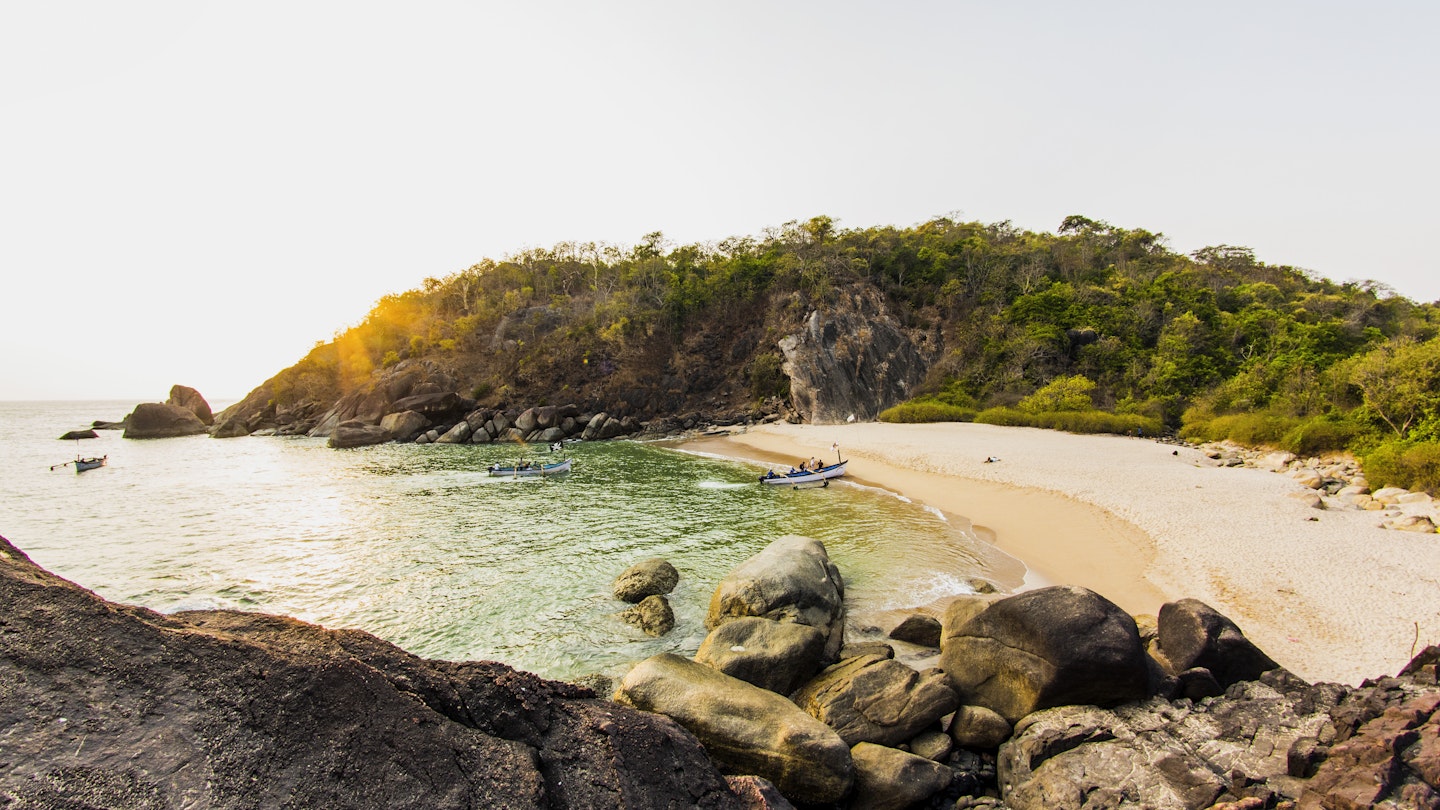Butterfly Island: a crescent of beach with a single canoe moored on the sand, two more canoes are in the sea approaching the beach. Behind the beach is dense jungle.
