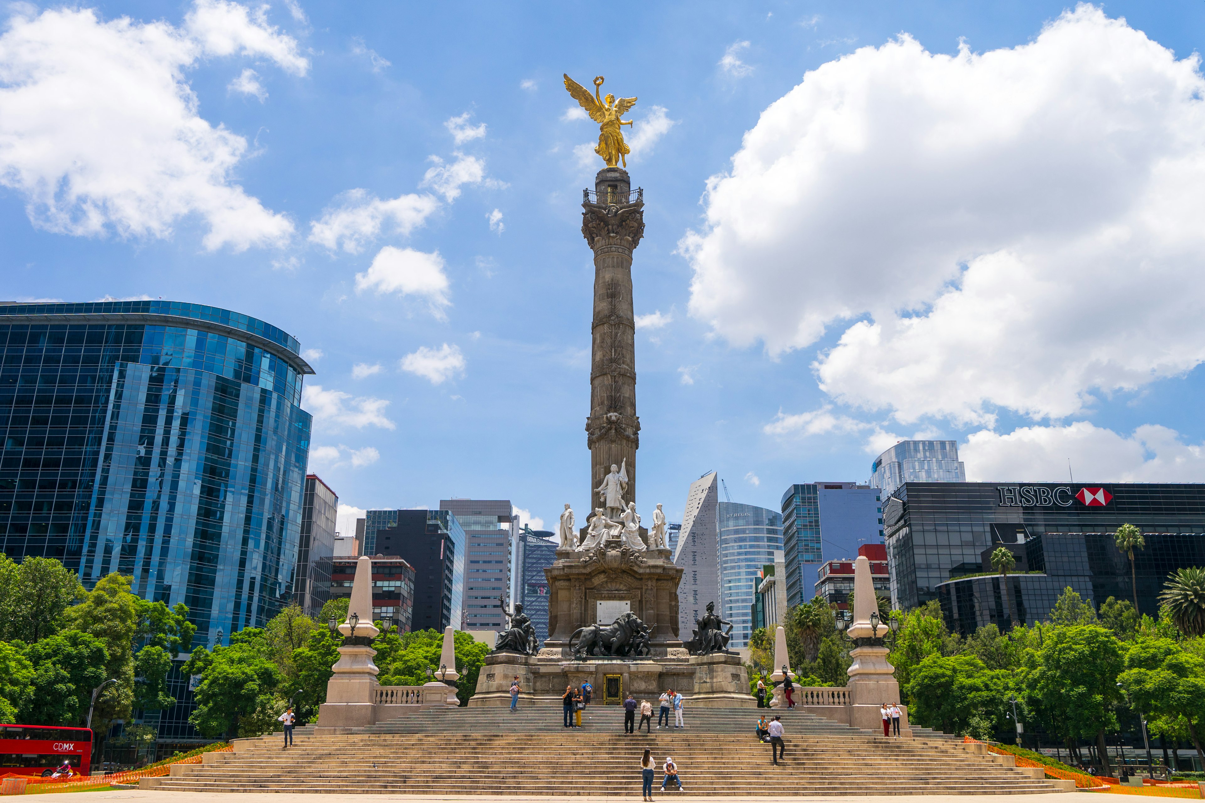 An obelisk topped with a golden angel stands surrounded by high rises