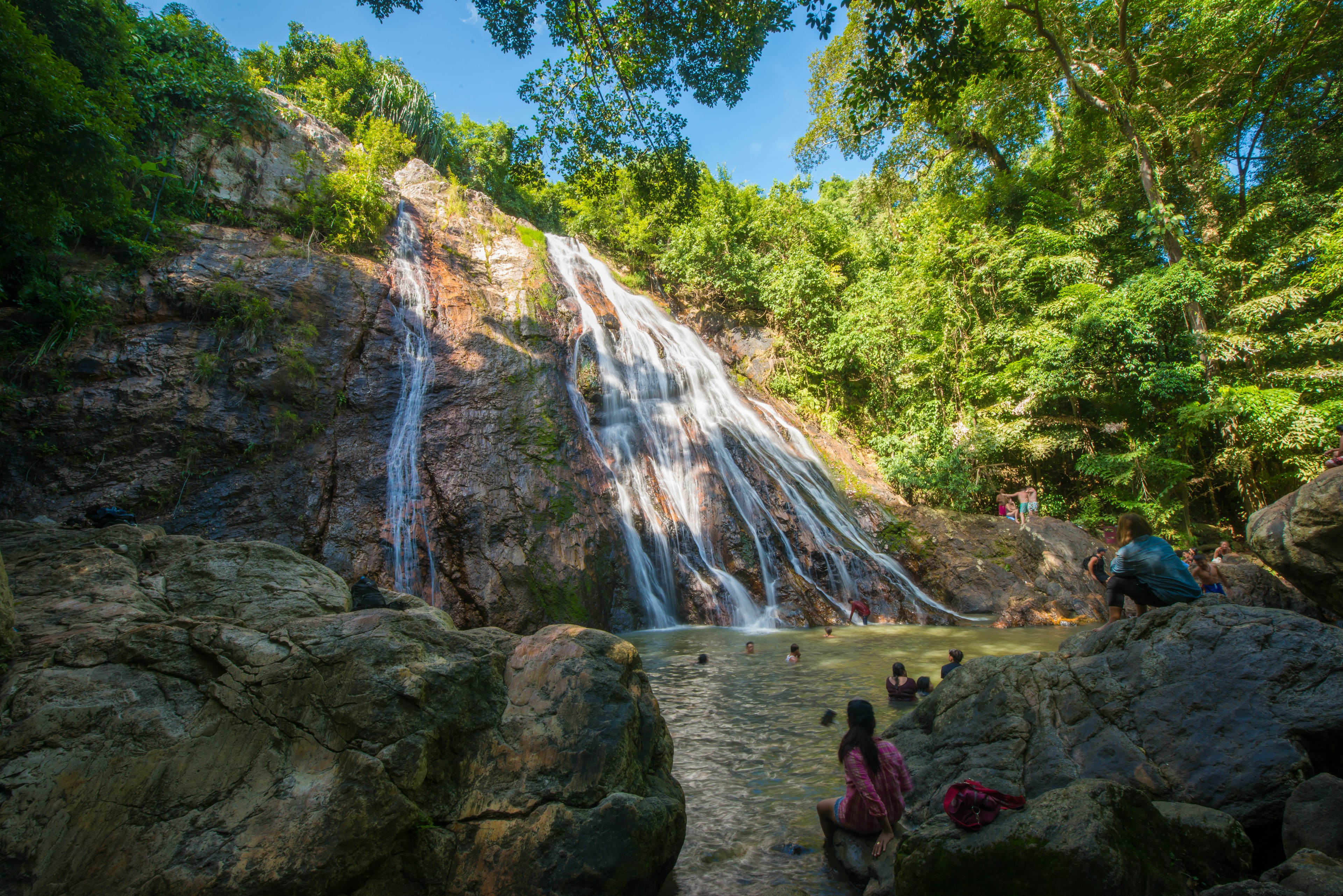 People swim in a pool at the foot of a waterfall