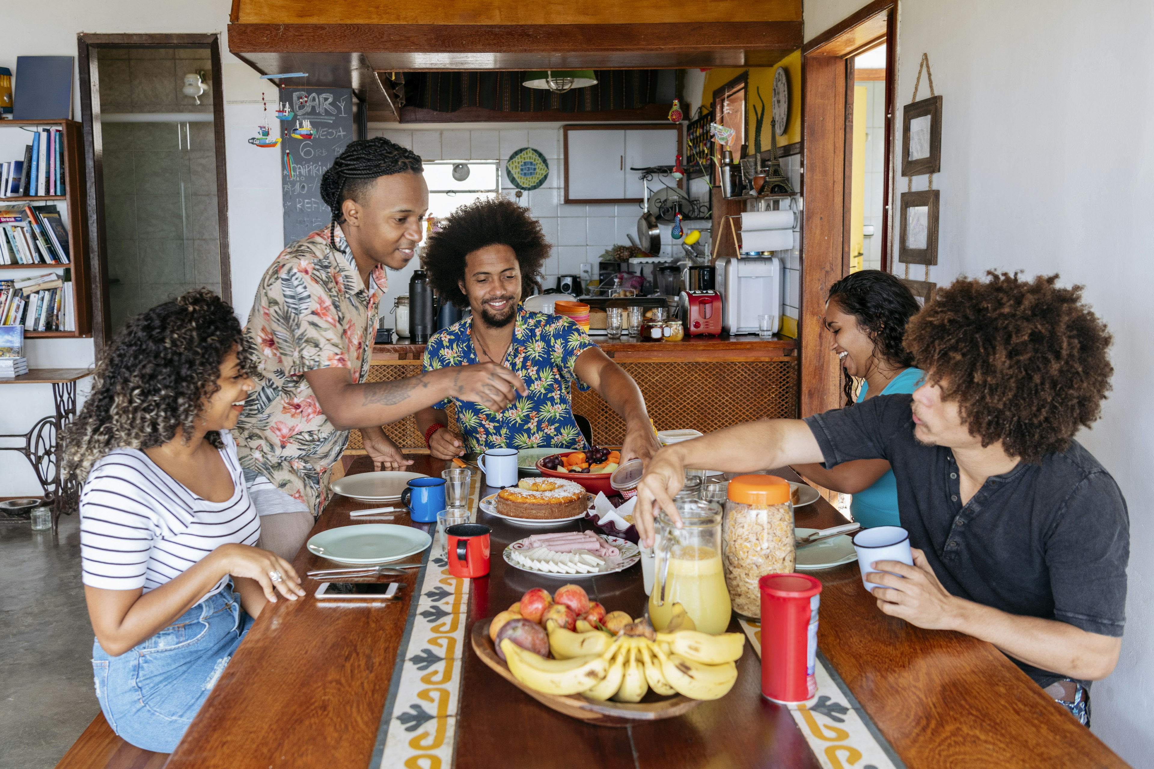 A group of five people eat at a table in a hostel common room