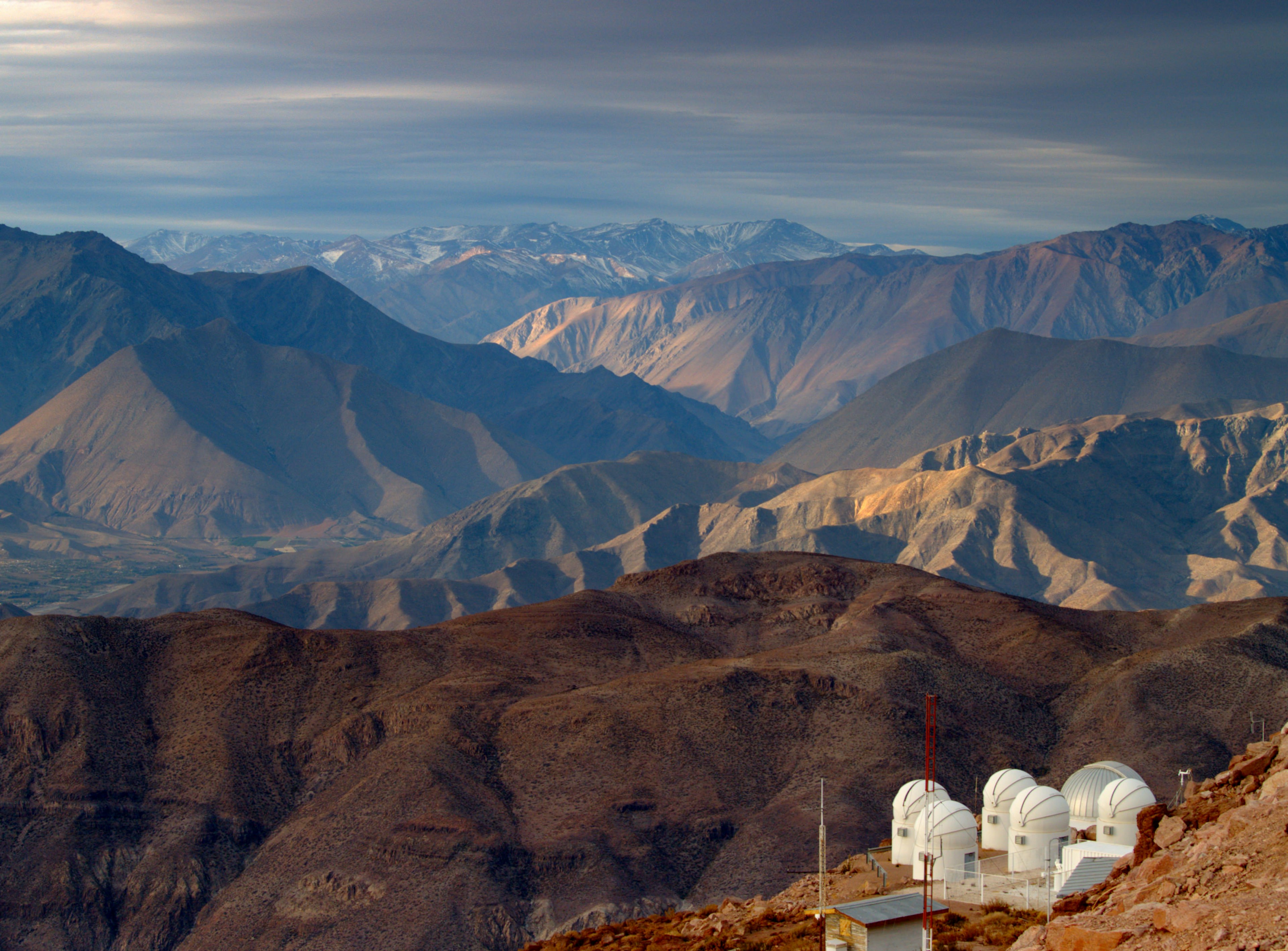 A view of a brown, rocky mountain range with an observatory in the foreground