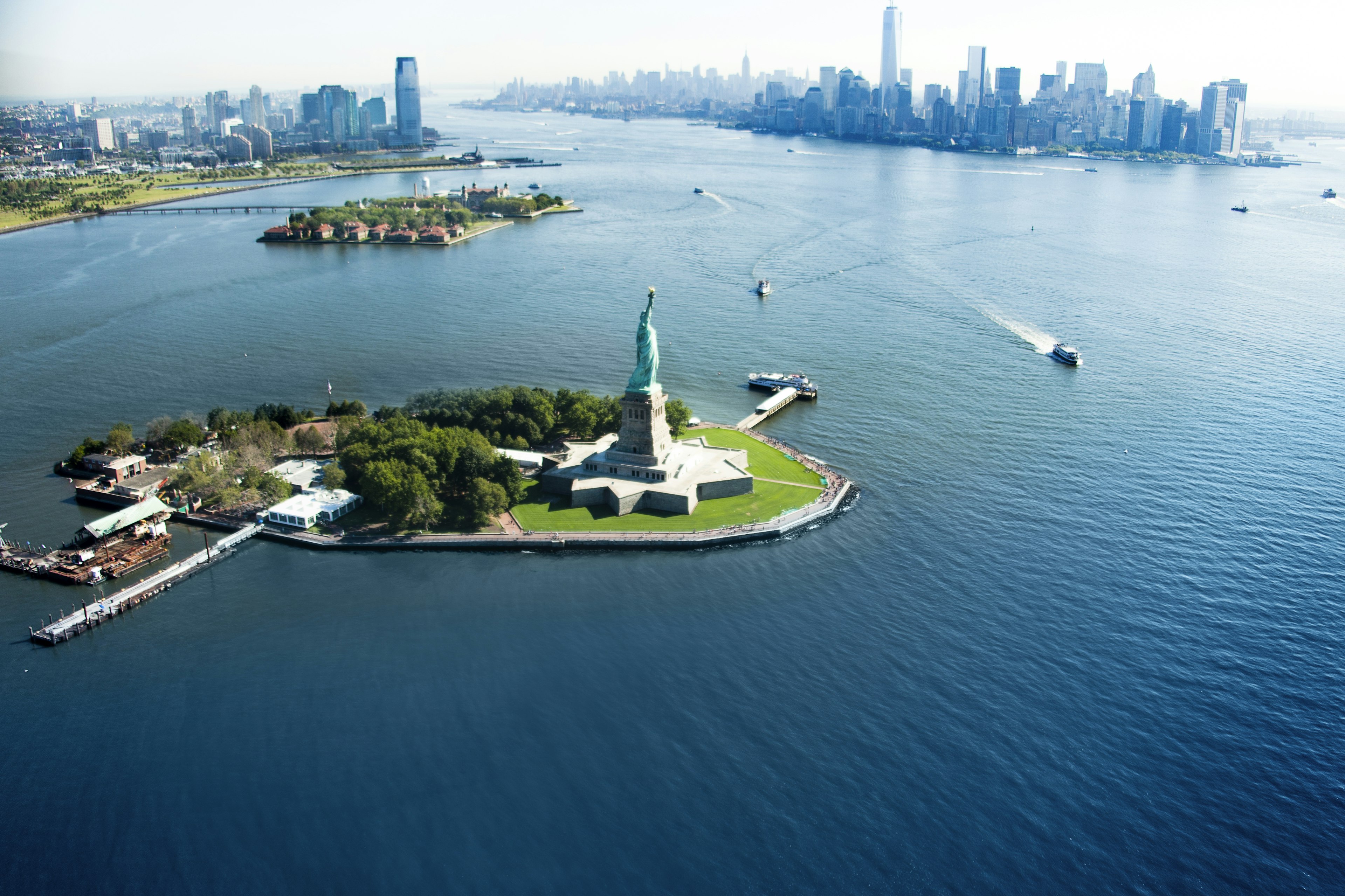 An aerial view of a statue on an island with a city skyline behind.