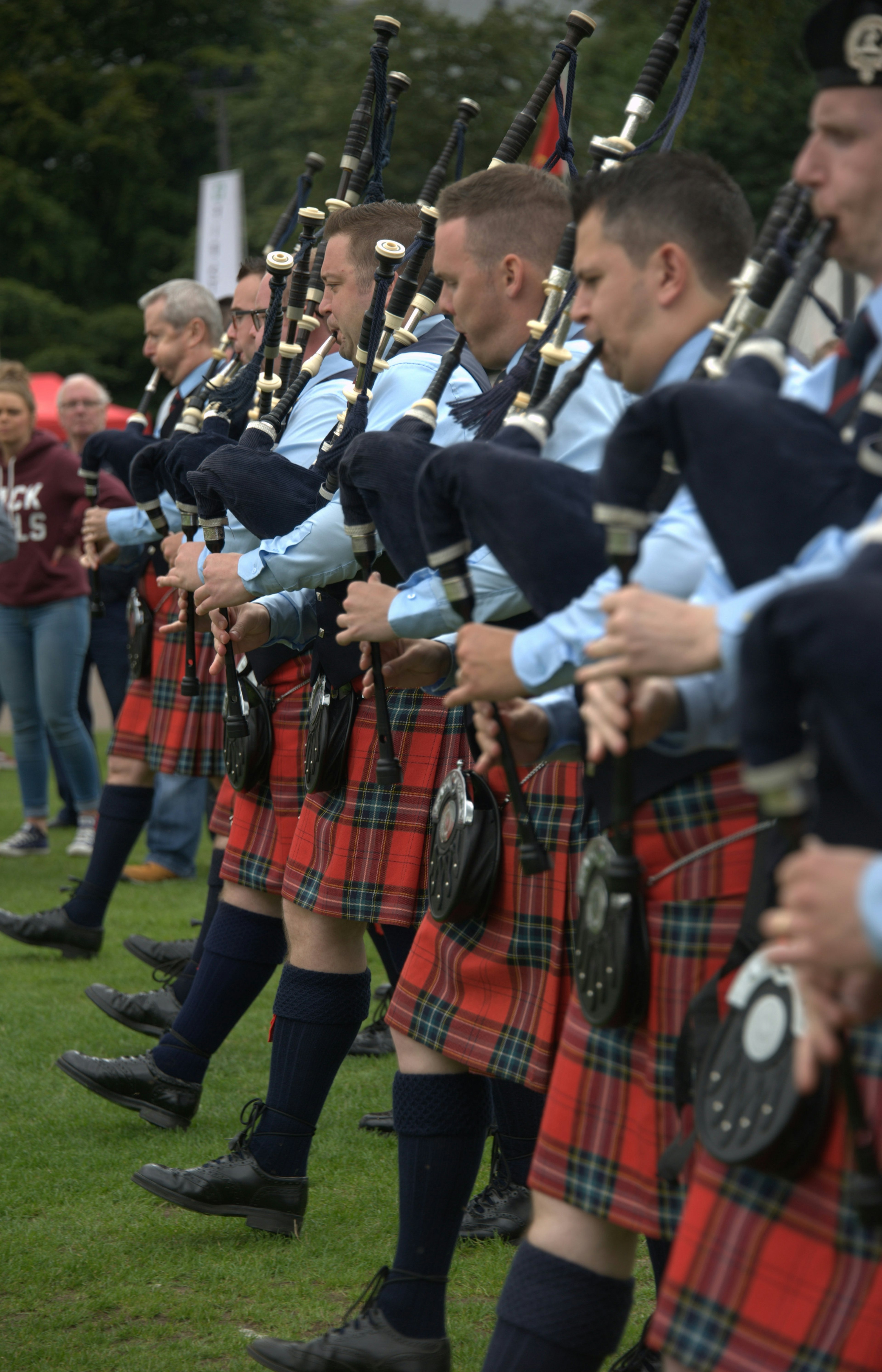 Pipers/bagpipers/bagpipe players with kilts walk in a line on the grass at the world pipe band championships.