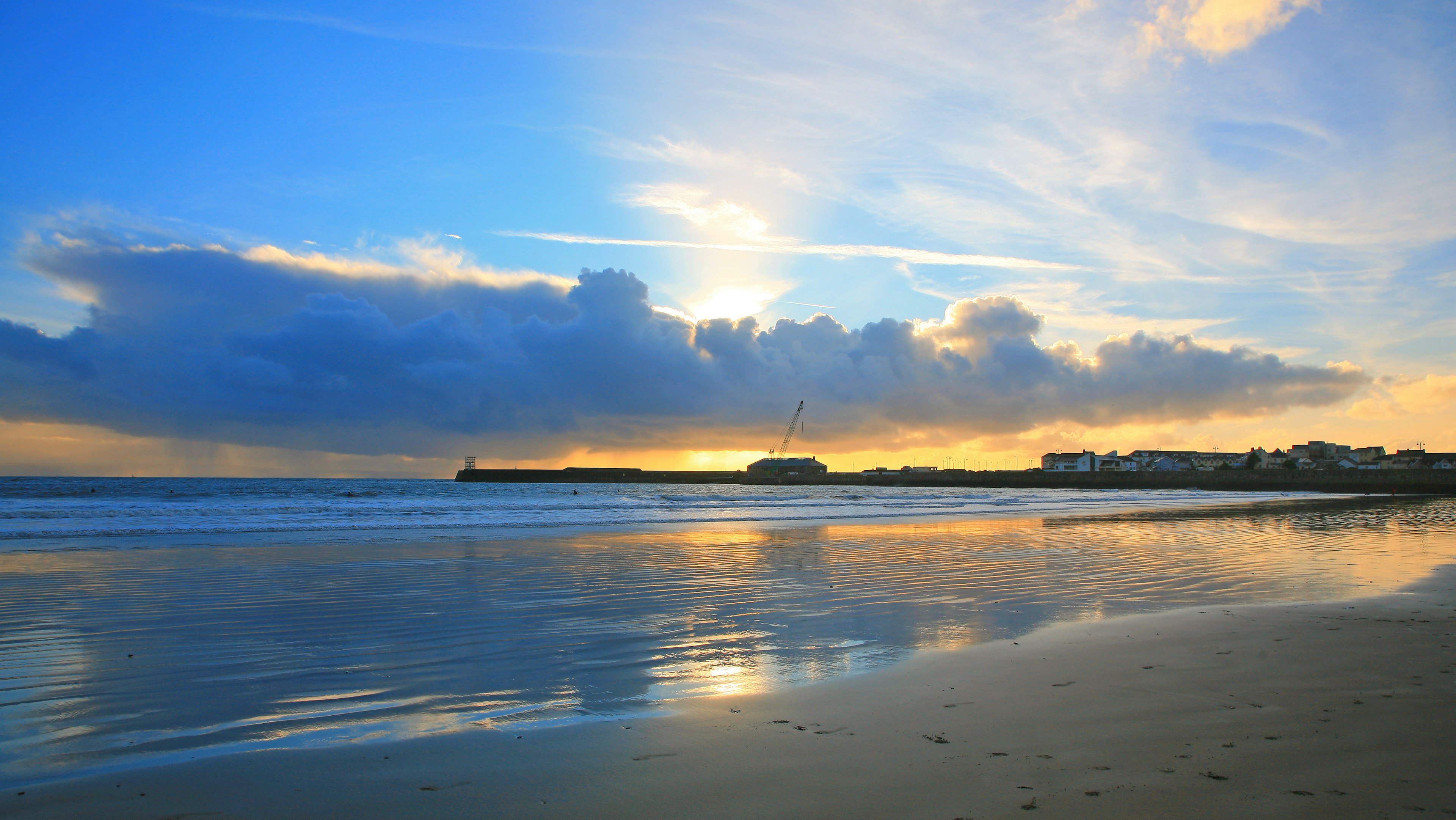 Sunset over beach reflecting in the wet sand with headland in the distance.