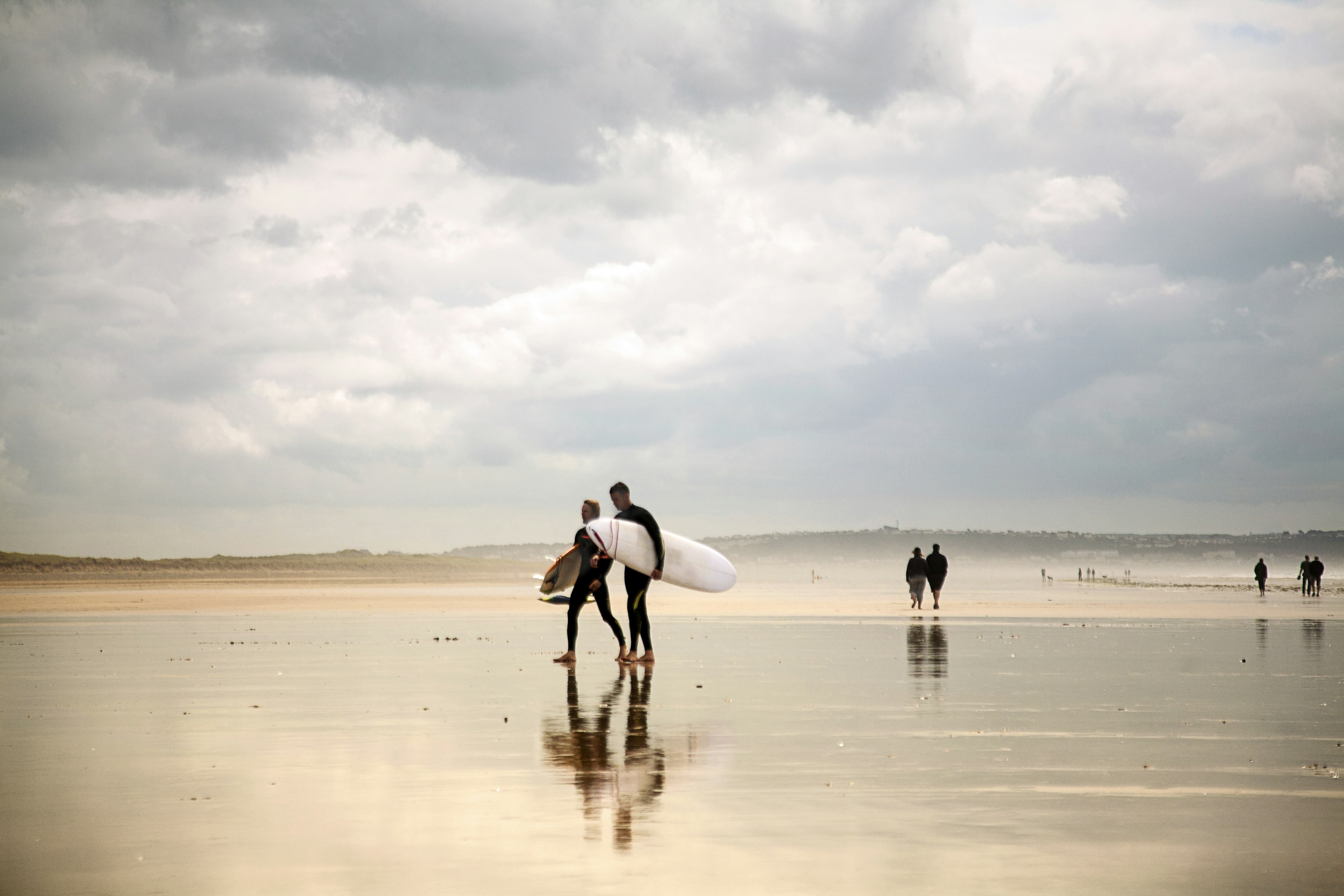 Two surfers carrying surfboards on Saunton Beach, Devon, England, UK