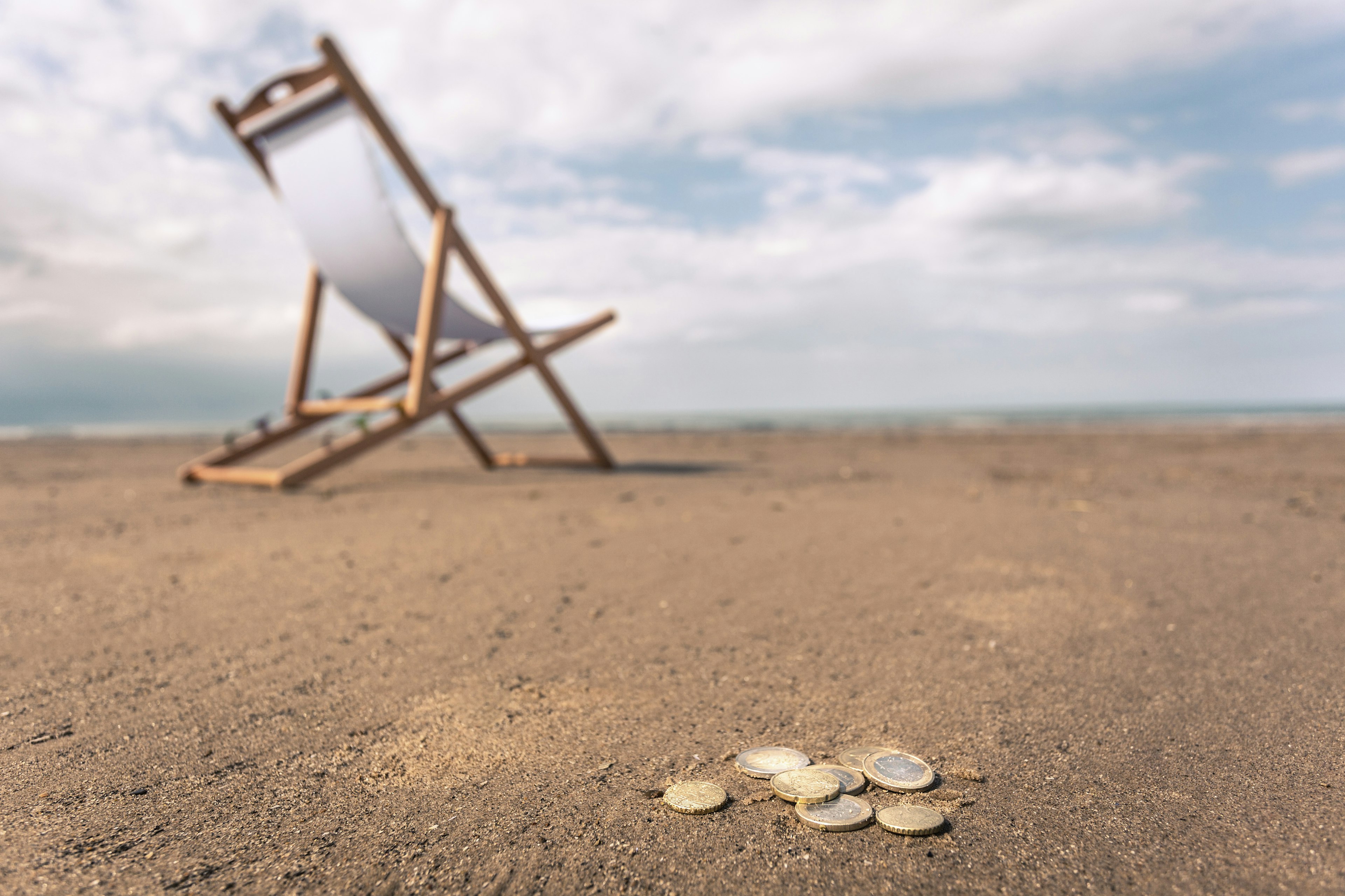 Deck chair on a Norfolk beach with coins on the sand in the foreground.