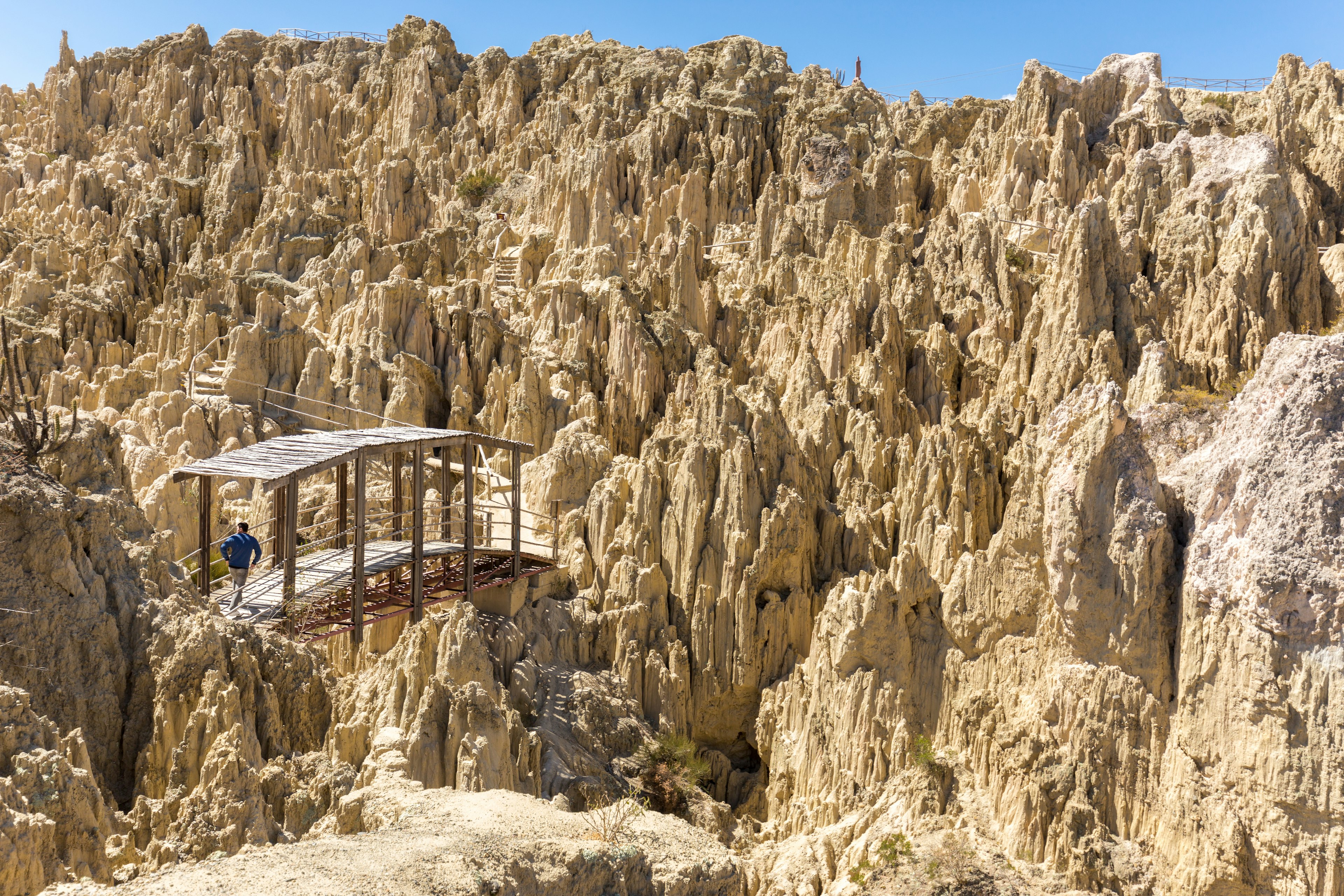 A person crosses a wood bridge among jagged geological formations in Valle de la Luna. La Paz, Bolivia.