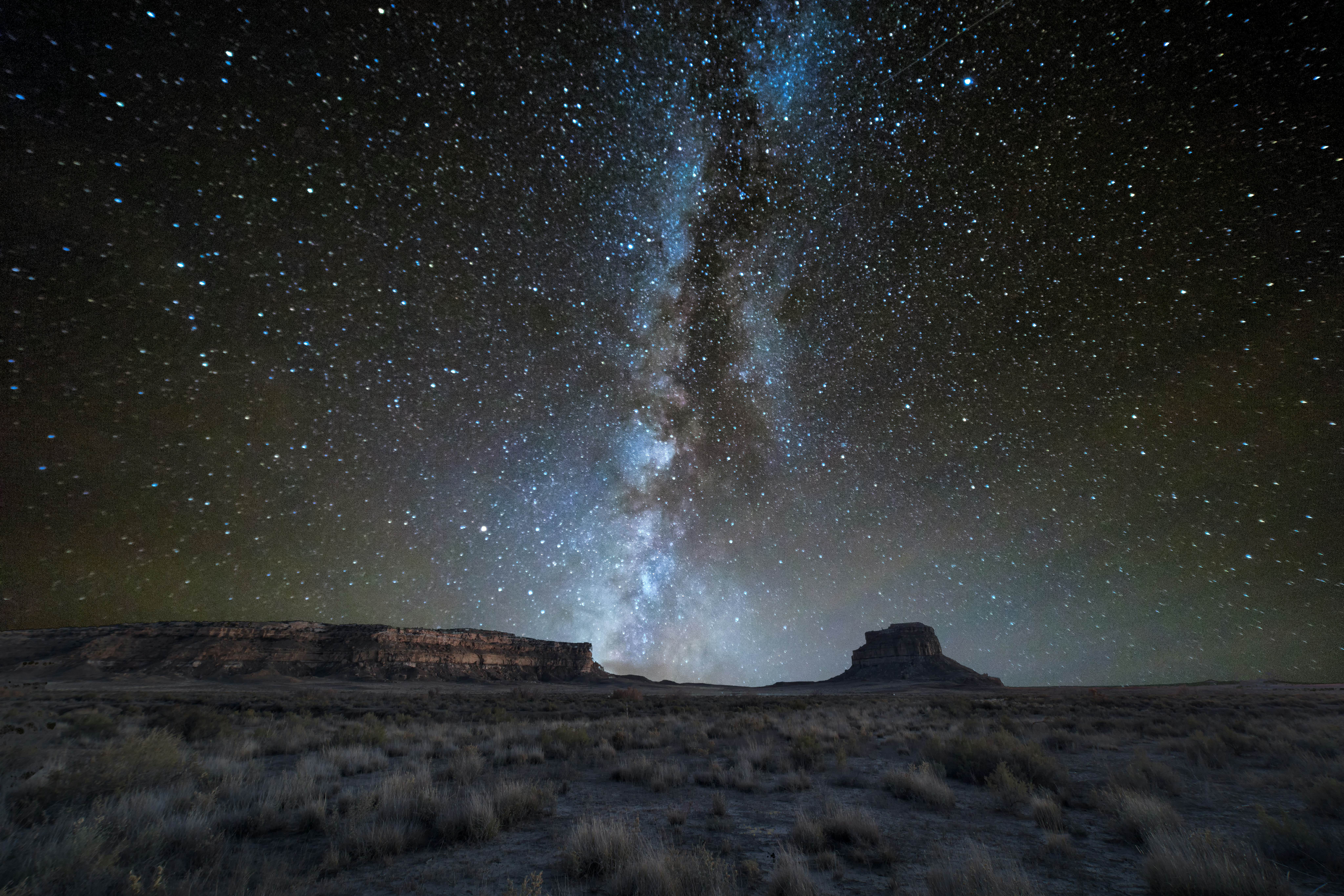 The Milky Way galaxy -- a thick band of stars that form a white line -- over rock formations in a canyon