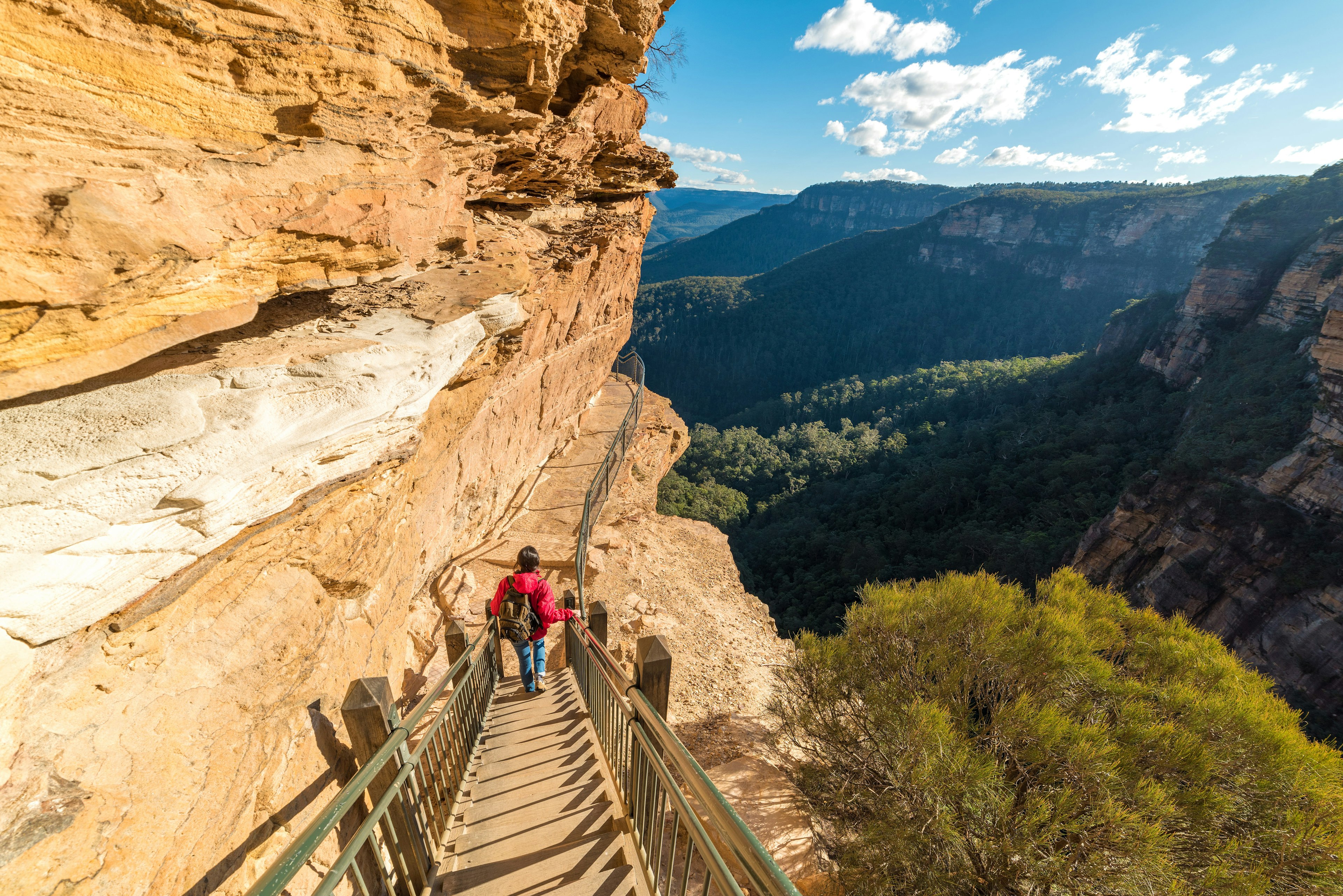 A woman walks down a path carved into a steep rock face in Blue Mountains National Park, New South Wales, Australia