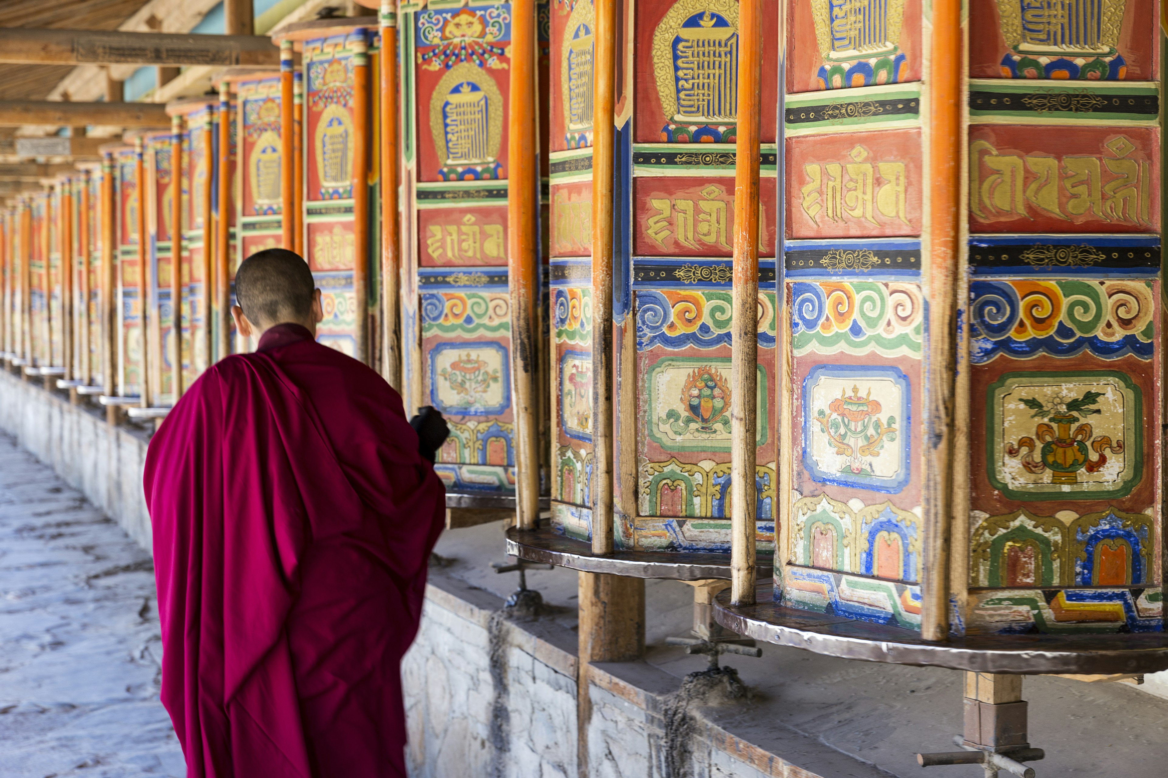 A monk is walking and turning huge, colorful prayer wheels in the Labrang monastery in Xiahe, Gansu province.