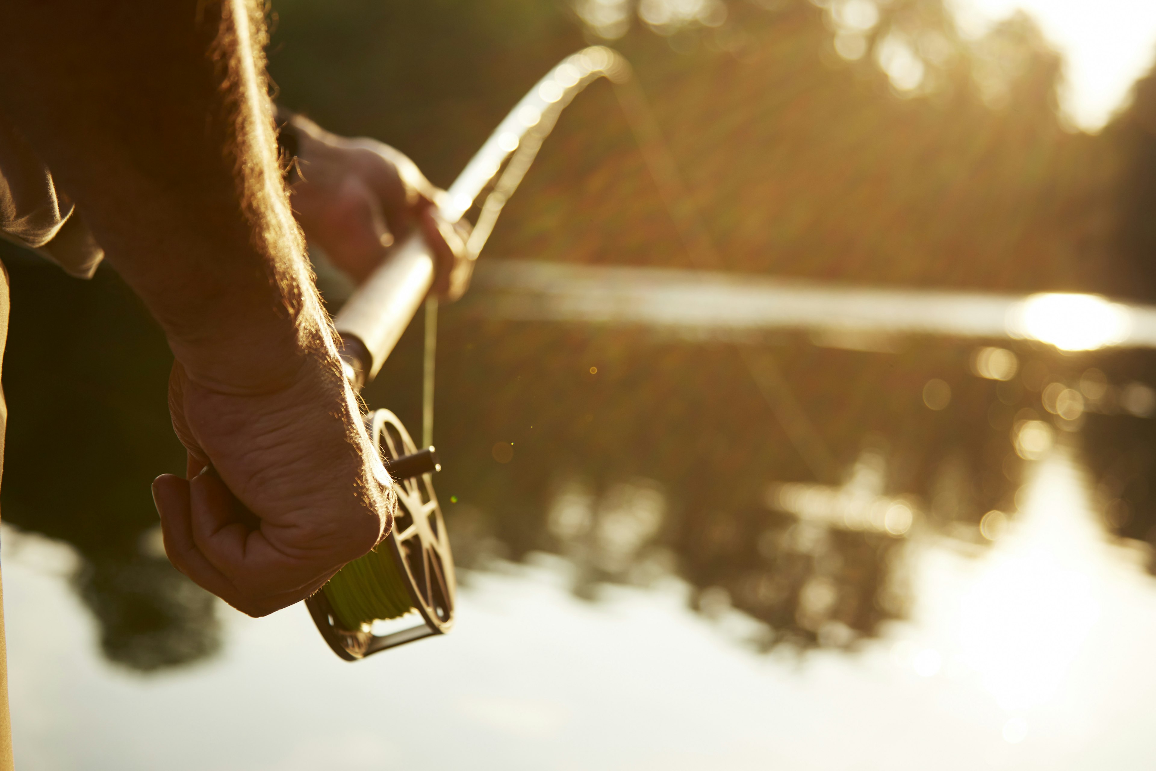 Close-up of a man's hands holding a fly fishing rod at a sunny lake. 