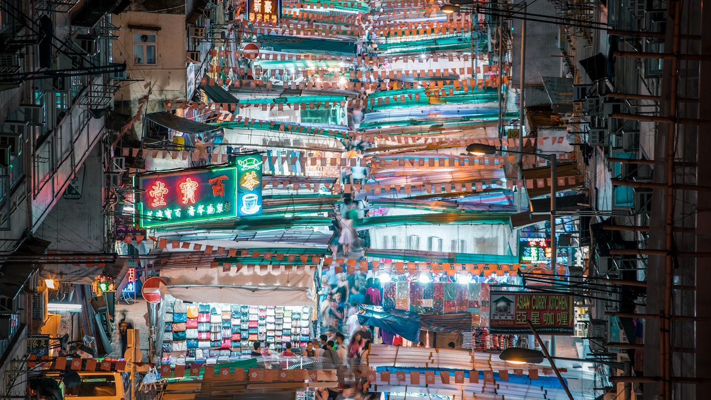 An overhead shot numerous brightly lit shopping stalls in a street market in Mong Kok, Hong Kong.