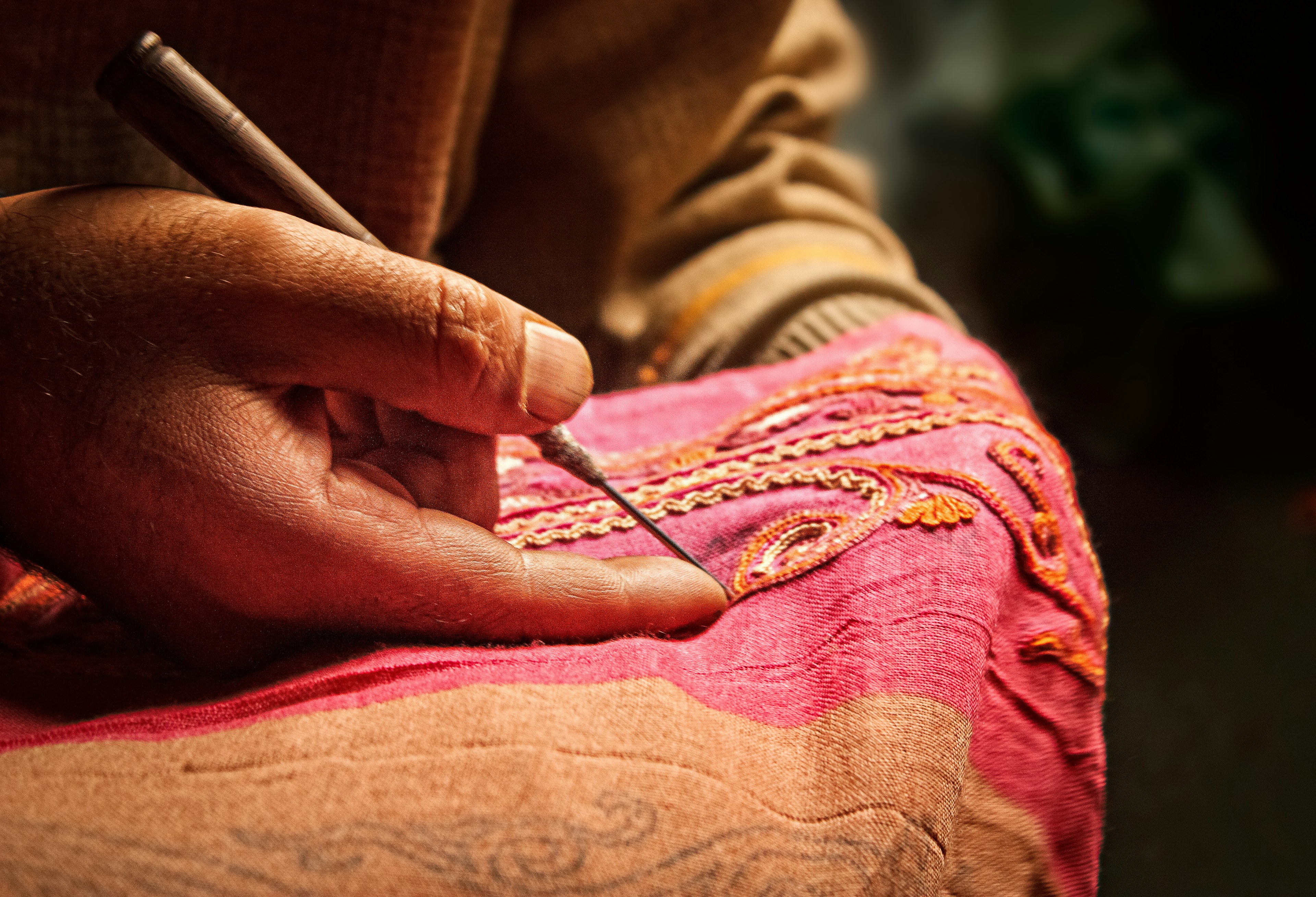 Kashmiri man uses an Aar needle to form Aari Embroidery on a pink scarf, a traditional form of embroidery from Kashmir.