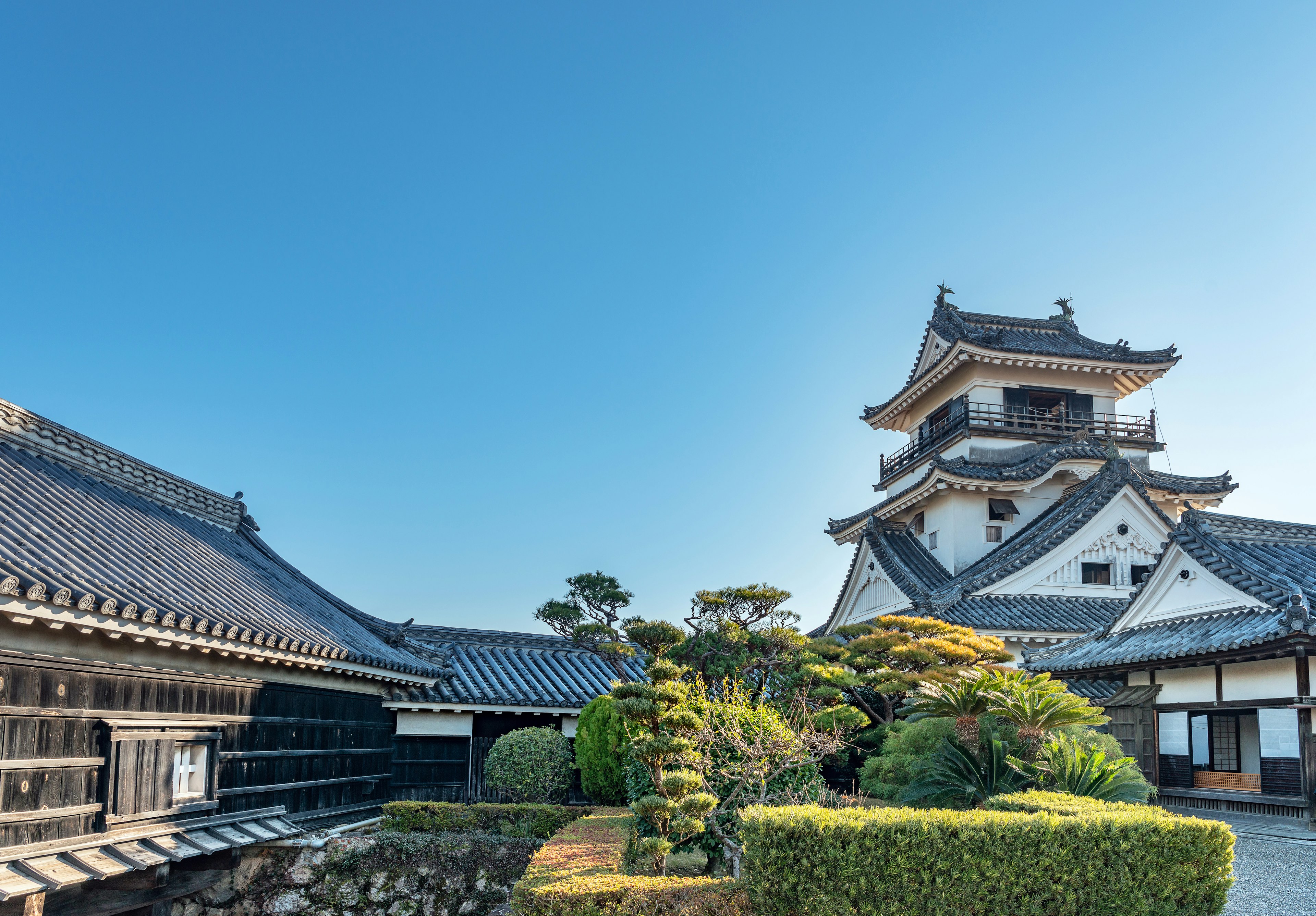 A traditional Japanese castle surrounded by bushes and trees on a bright, sunny day.