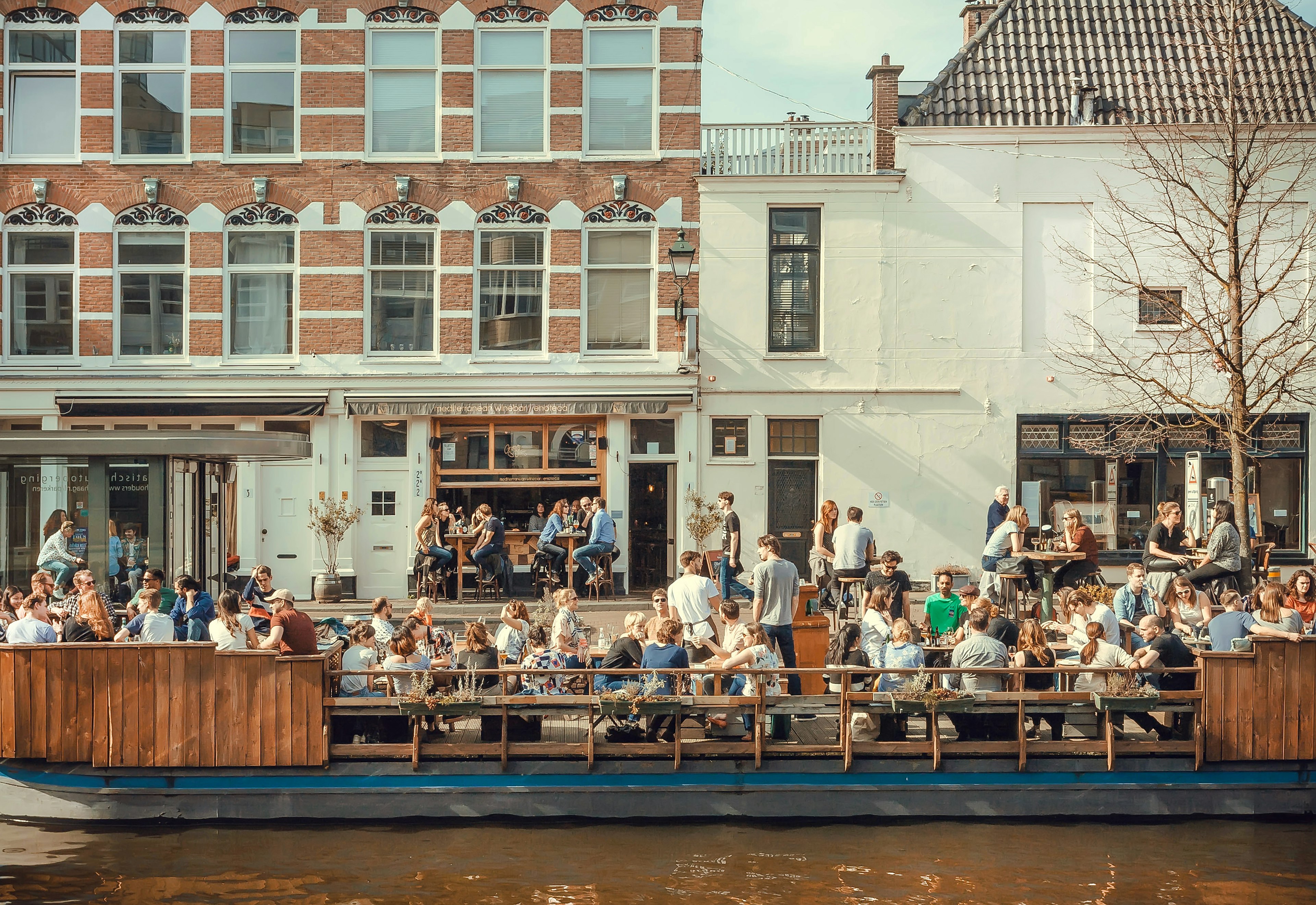 People eating and talking on a riverboat cafe in the canal on a sunny day.