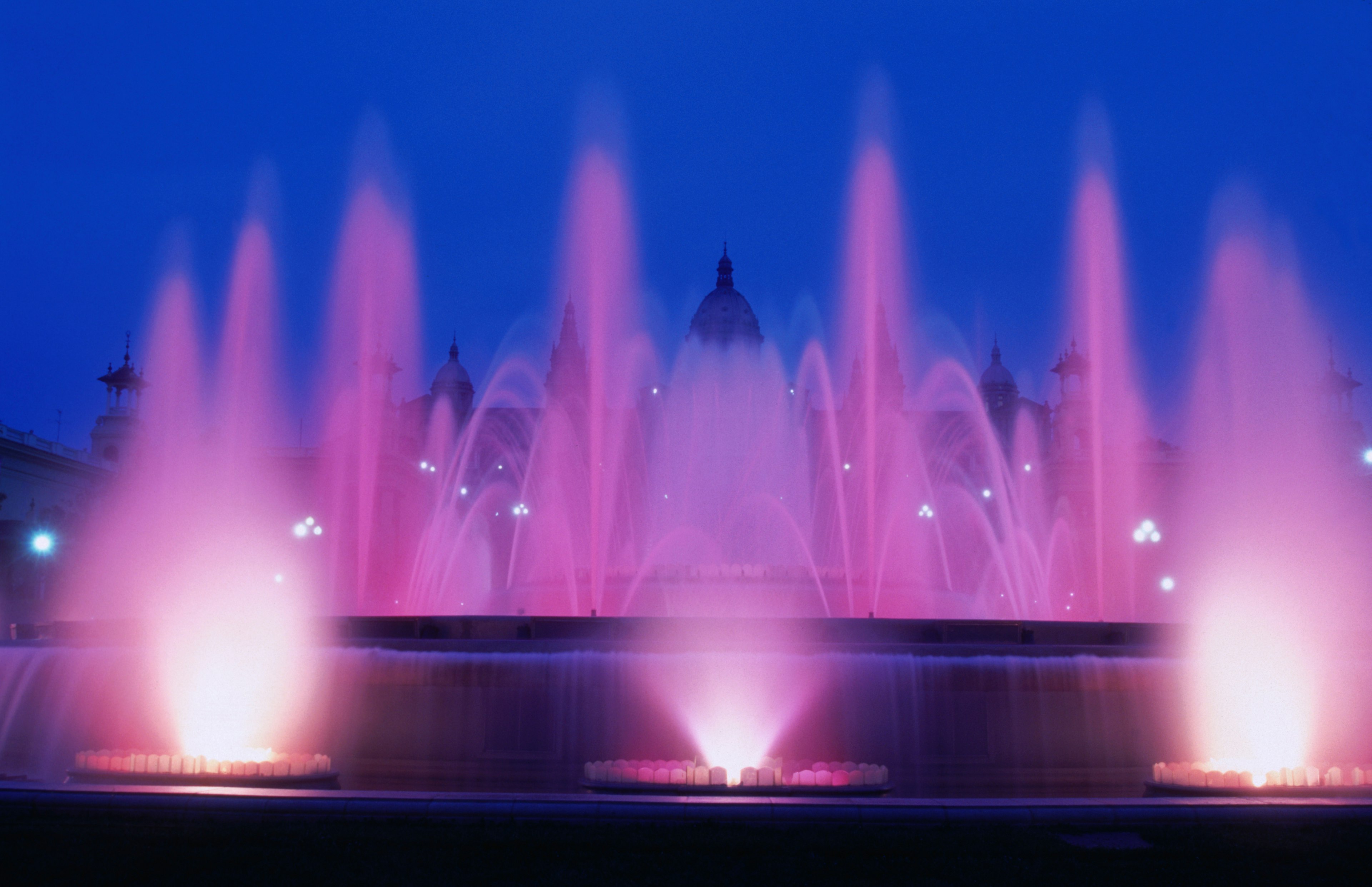 The fountain is lit up pink, with at least six jets of water shooting high into the sky, and many arcing over the fountain.