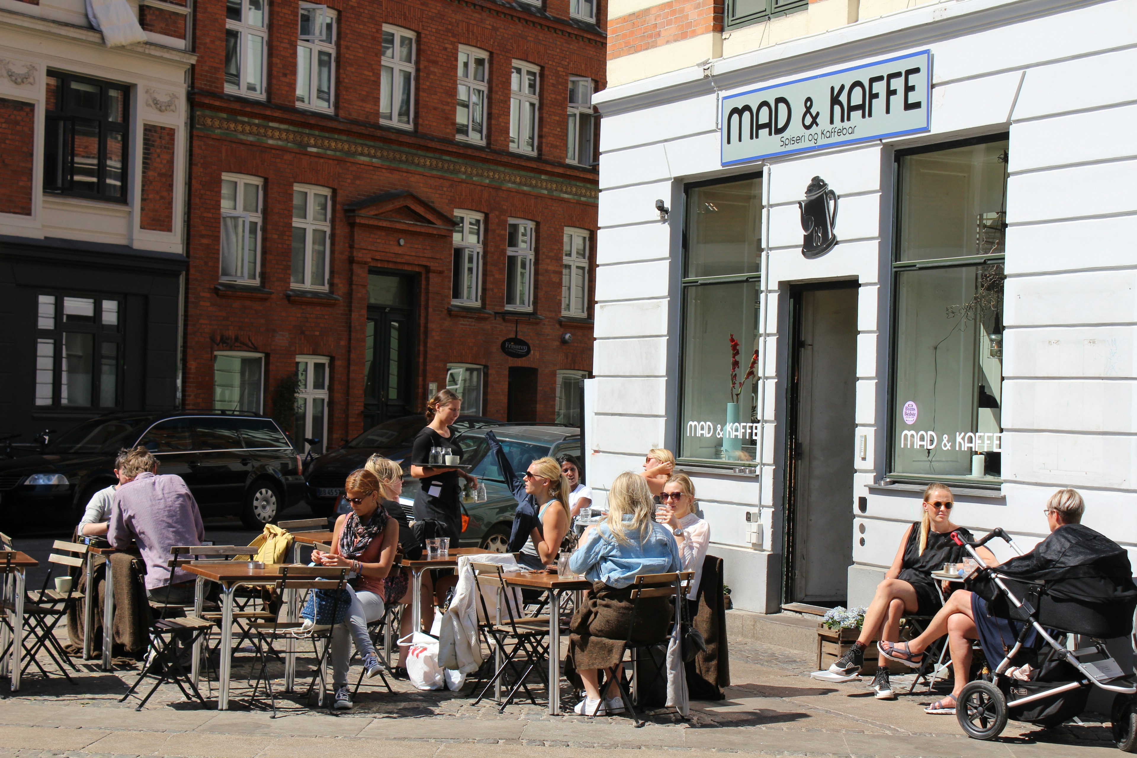 Mad & Kaffe, seen from the outside with many patrons lounging on the outside seating.