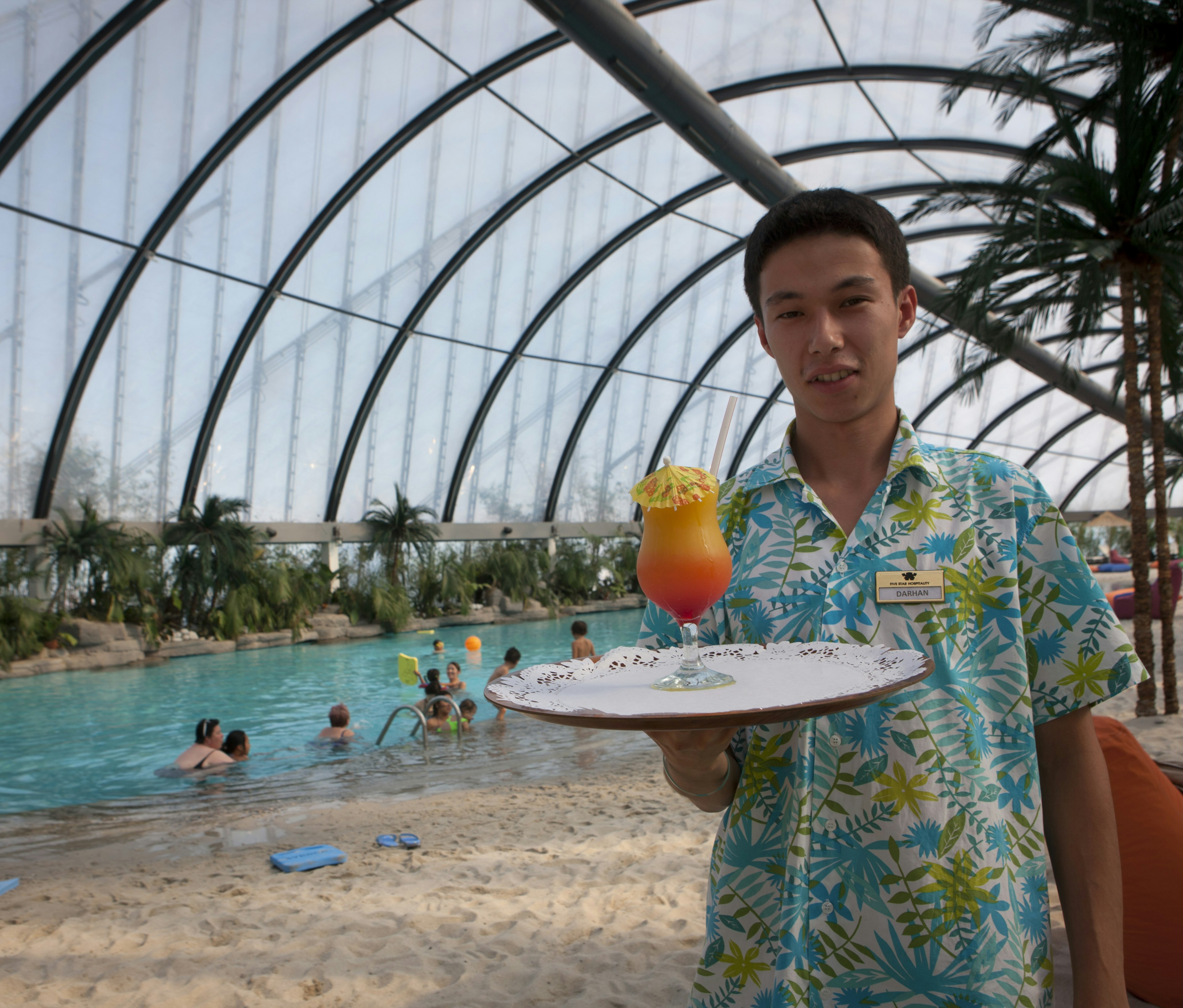 Waiter serving cocktail at covered beach pool in Khan Shatyr entertainment centre.