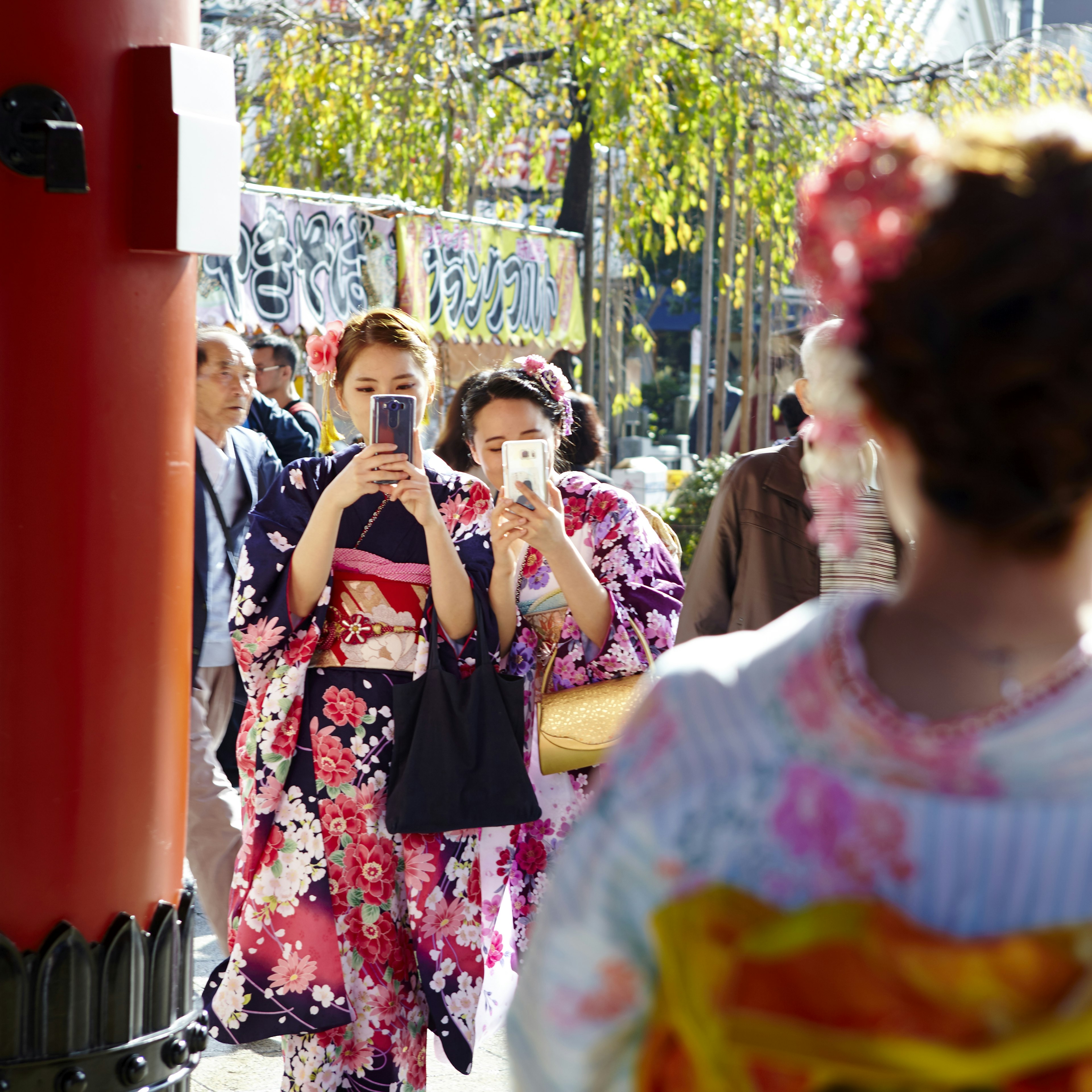 Women in flowery kimonos taking photos with smartphones