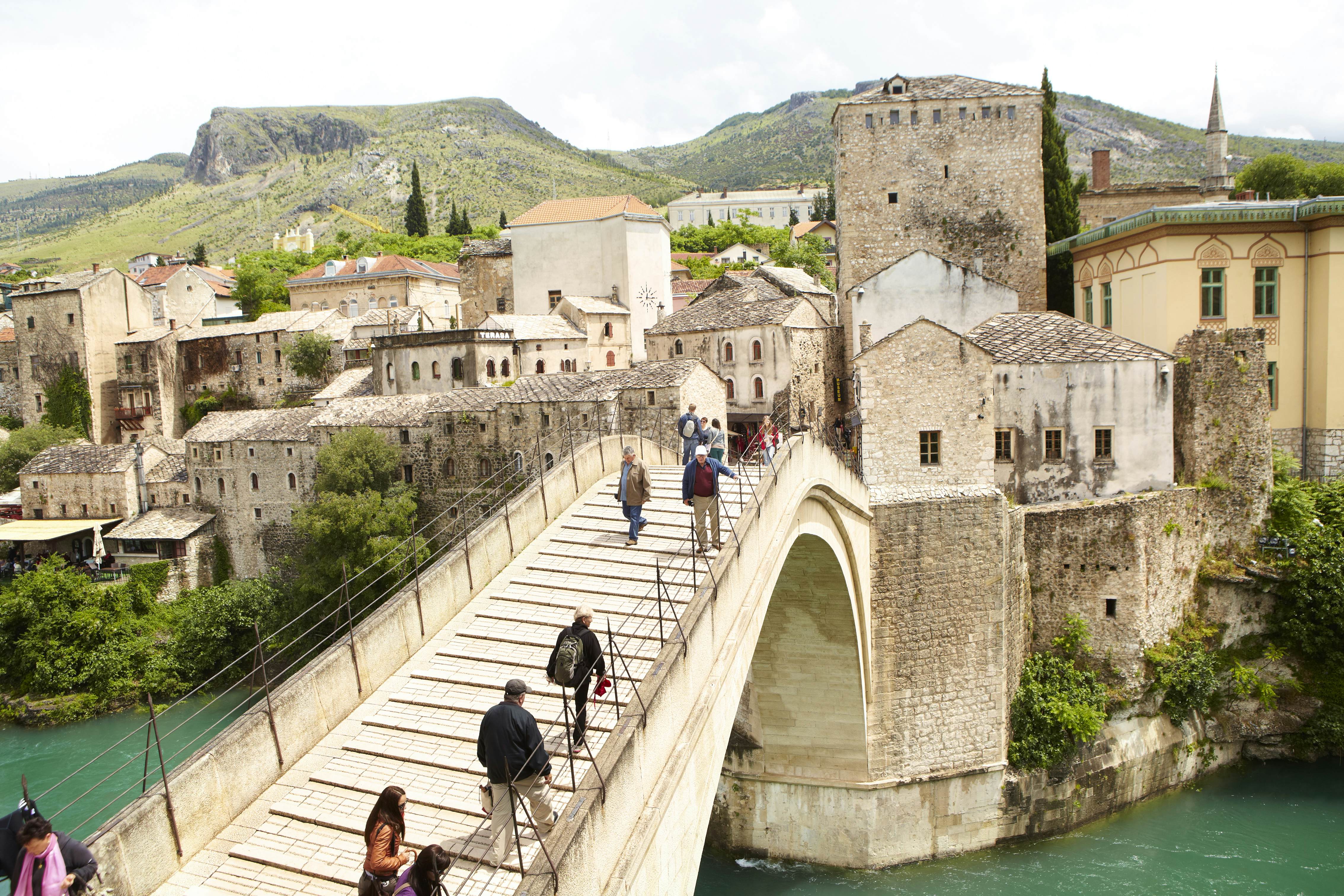 People walk along a beautiful bridge over a river in front of a historic town