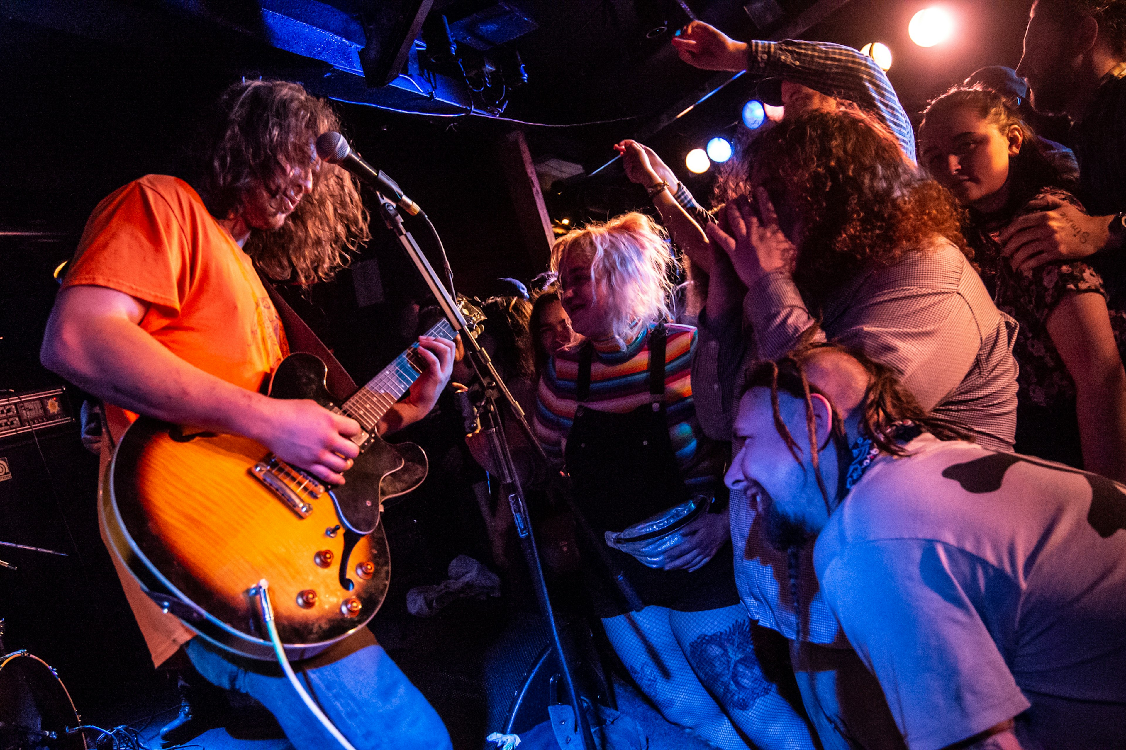 A bassist with long hair performs in close proximity to concertgoers in a rock club