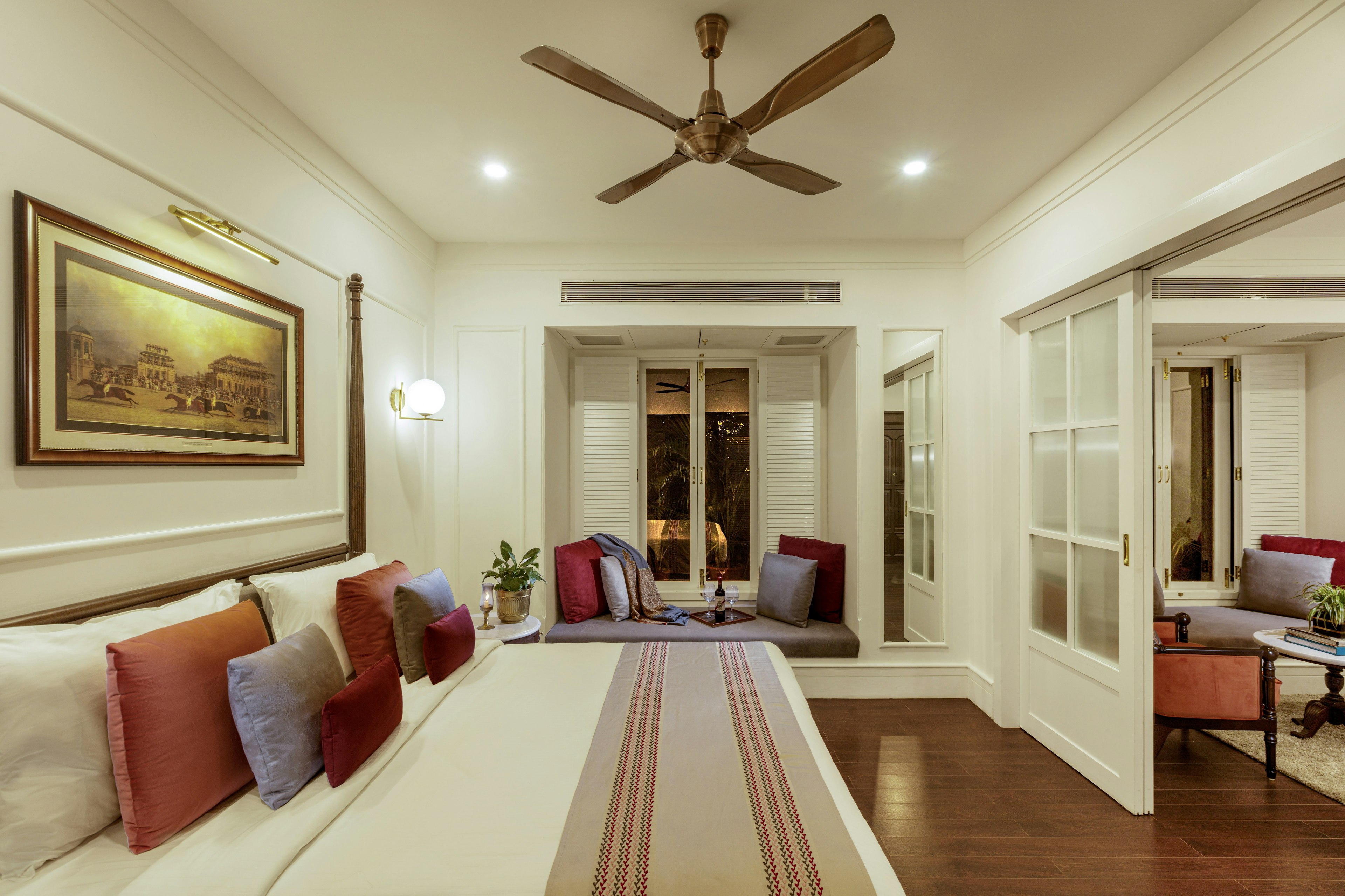 A hotel room immaculately furnished with a door opening onto a lounge area