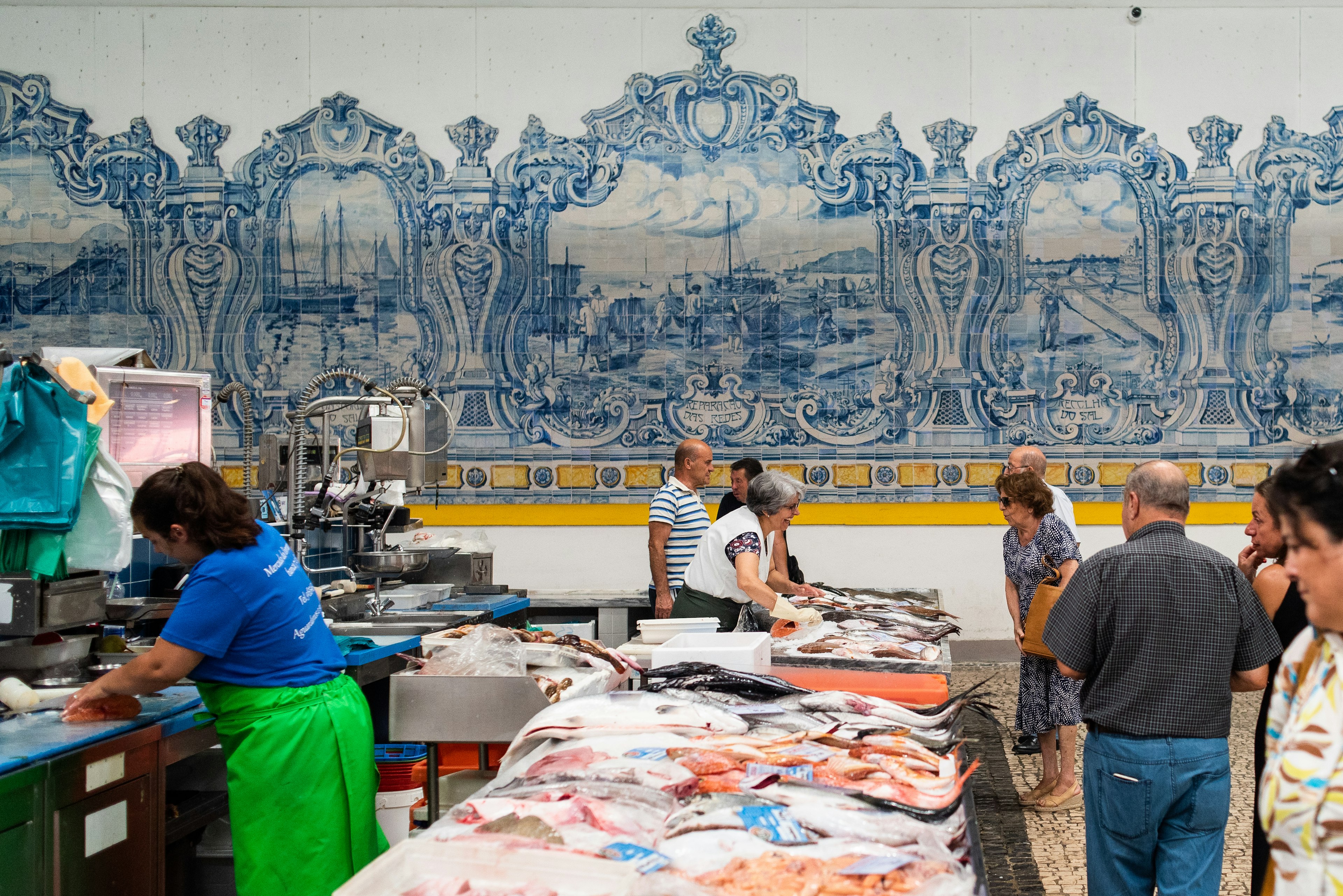 People look at fresh fish at a fish market with walls of blue-painted tile