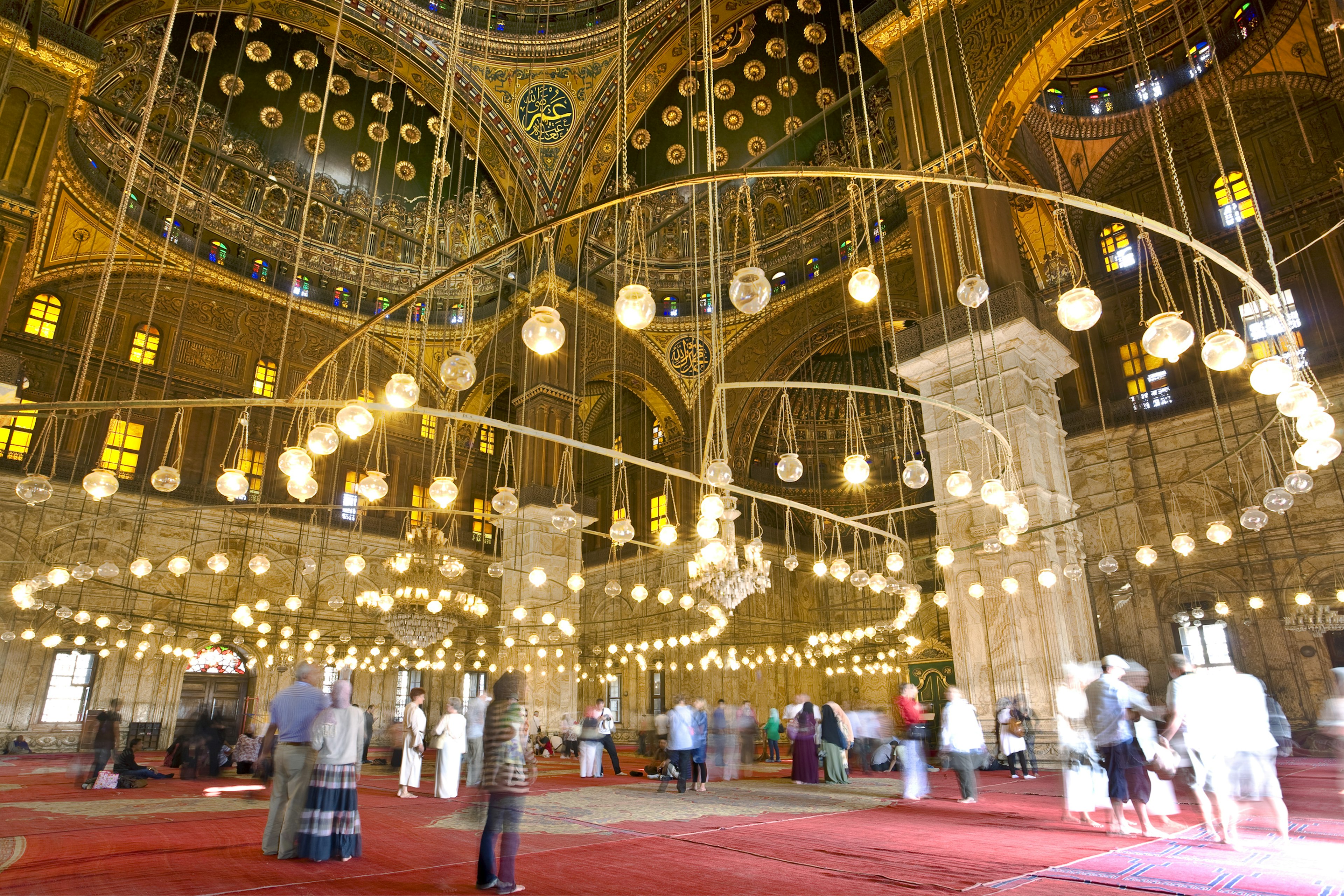 People admiring the chandeliers and ceilings of a vast mosque