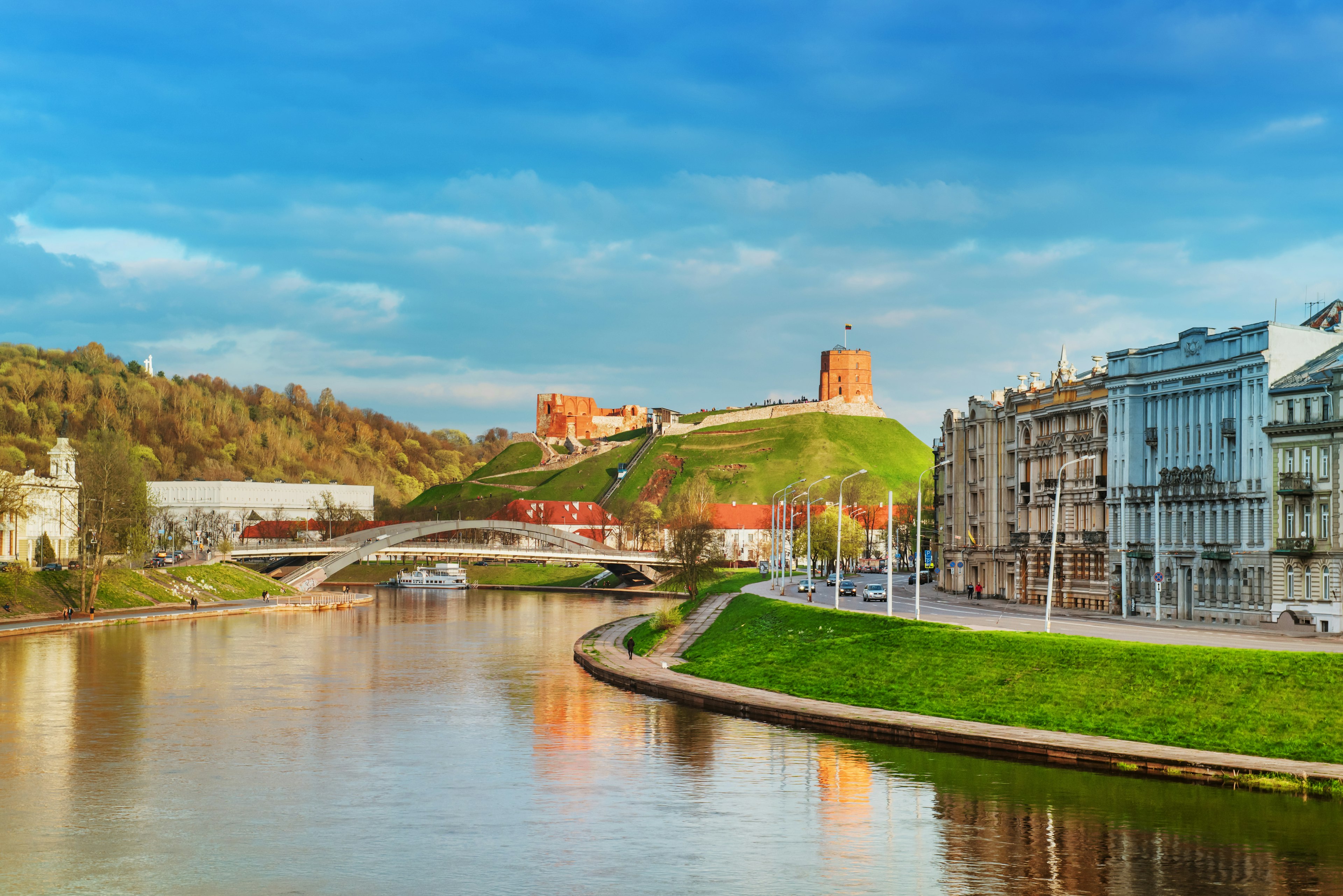 A red-brick castle on the top of a green hill by a river