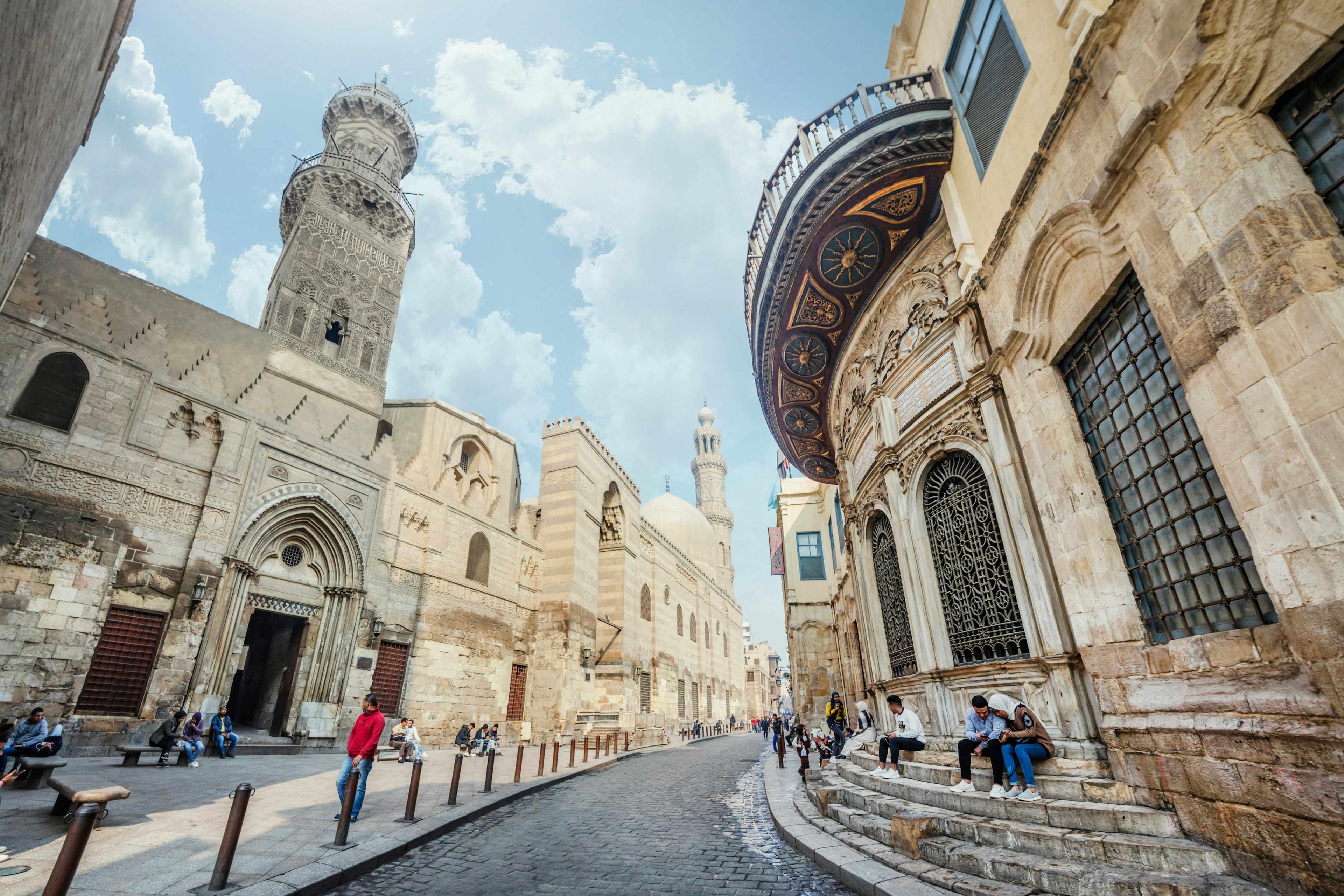 A narrow street lined with ancient buildings and a minaret rising above