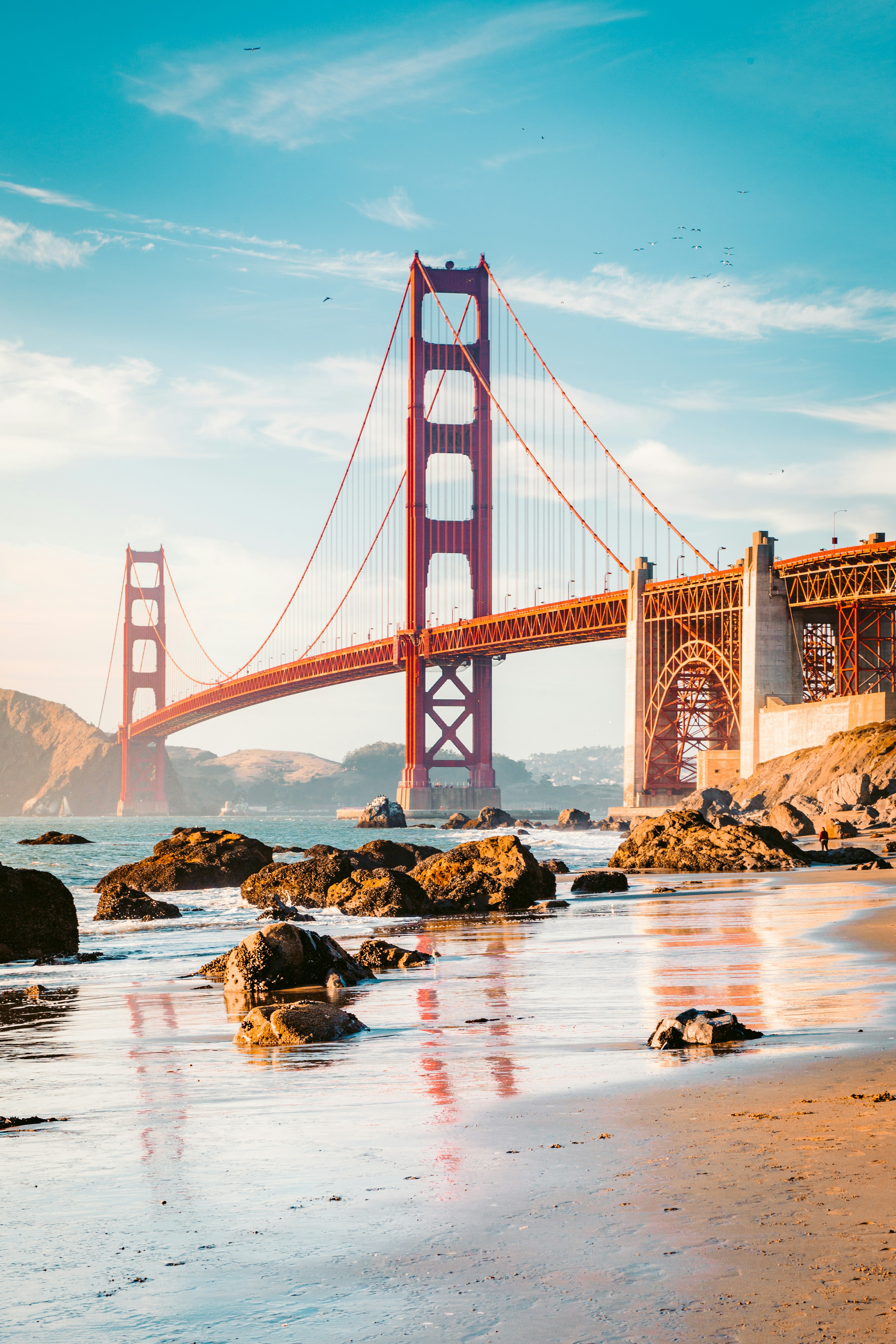 Classic panoramic view of famous Golden Gate Bridge seen from scenic Baker Beach in beautiful golden evening light on a sunny day with blue sky and clouds in summer, San Francisco, California.