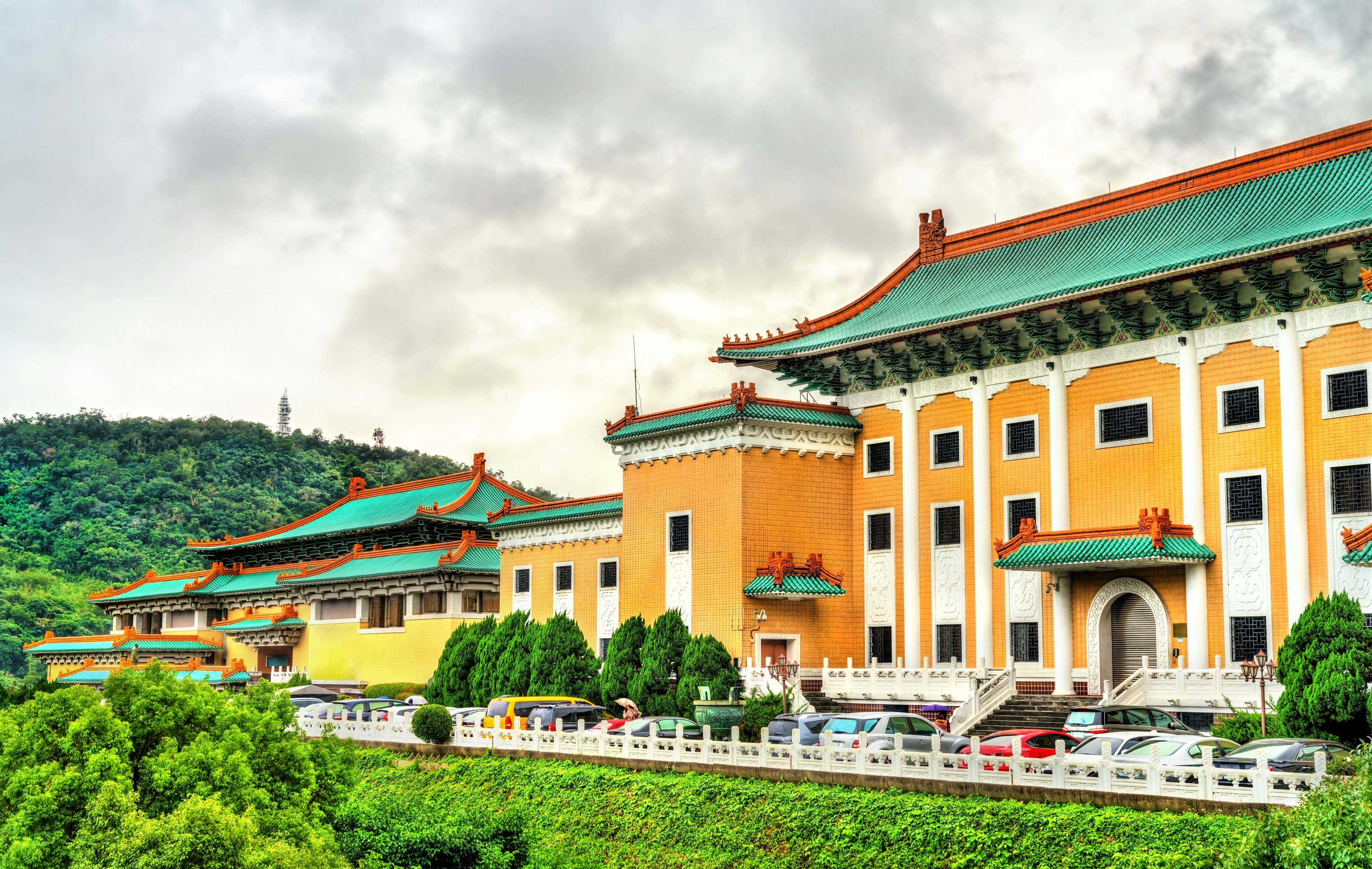 View of the National Palace Museum in Taipei, Taiwan. It's a gold, green and red building set into green hills.