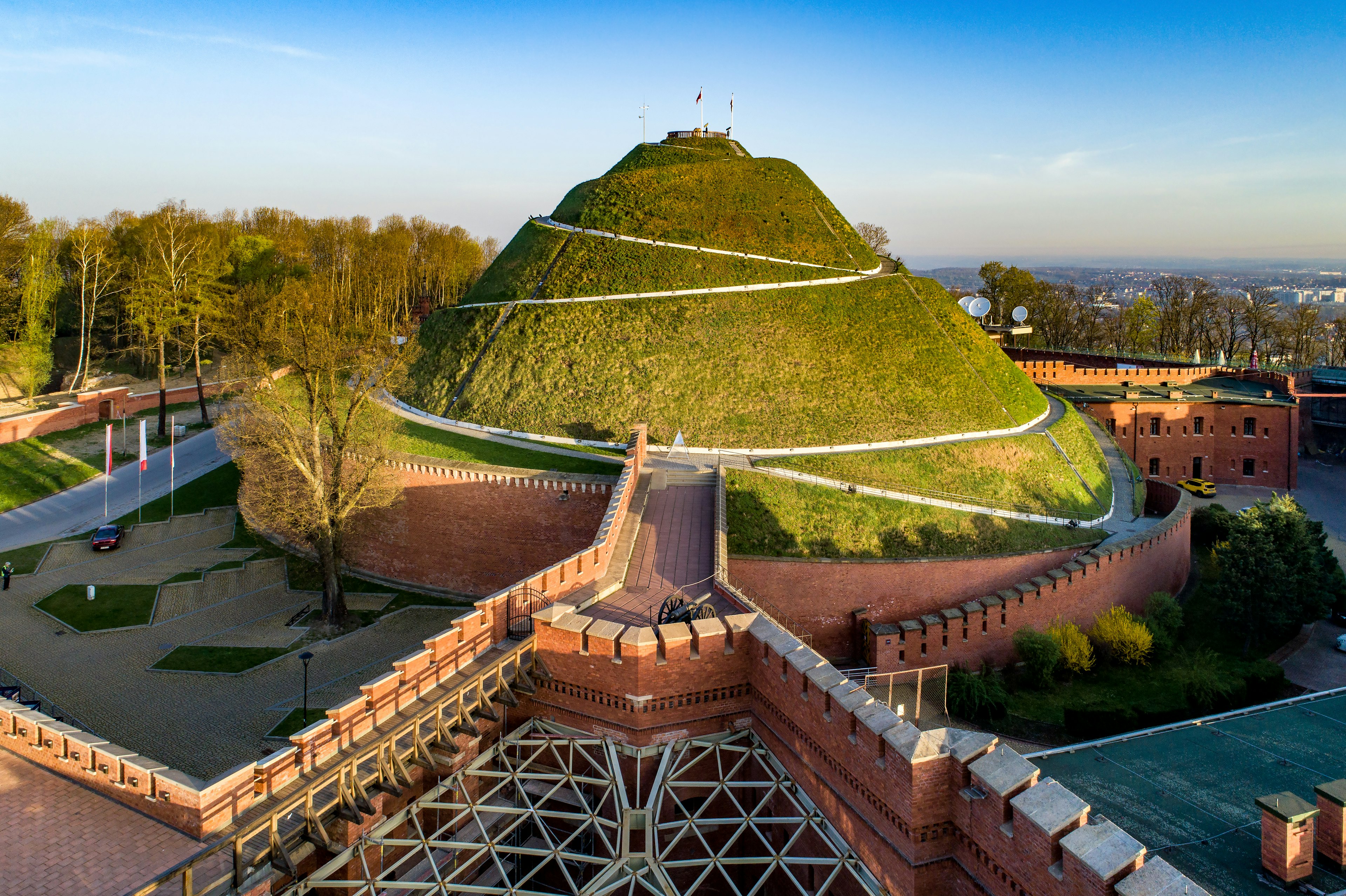 A giant green mound with a walkway is surrounded by a crenellated red-brick wall