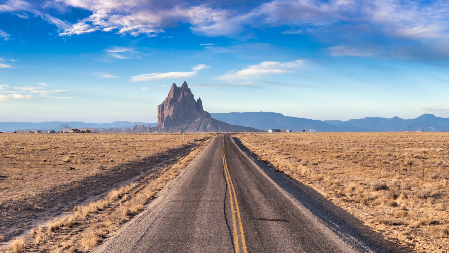 Panoramic View of a road in a dry desert with a Shiprock mountain peak in the background. Sunny and Cloudy Morning Sunrise Artistic Render. Taken at Rattlesnake, New Mexico, United States.  License Type: media  Download Time: 2023-09-01T03:37:46.000Z  User: aomi.ito_lonelyplanet  Is Editorial: No  purchase_order: