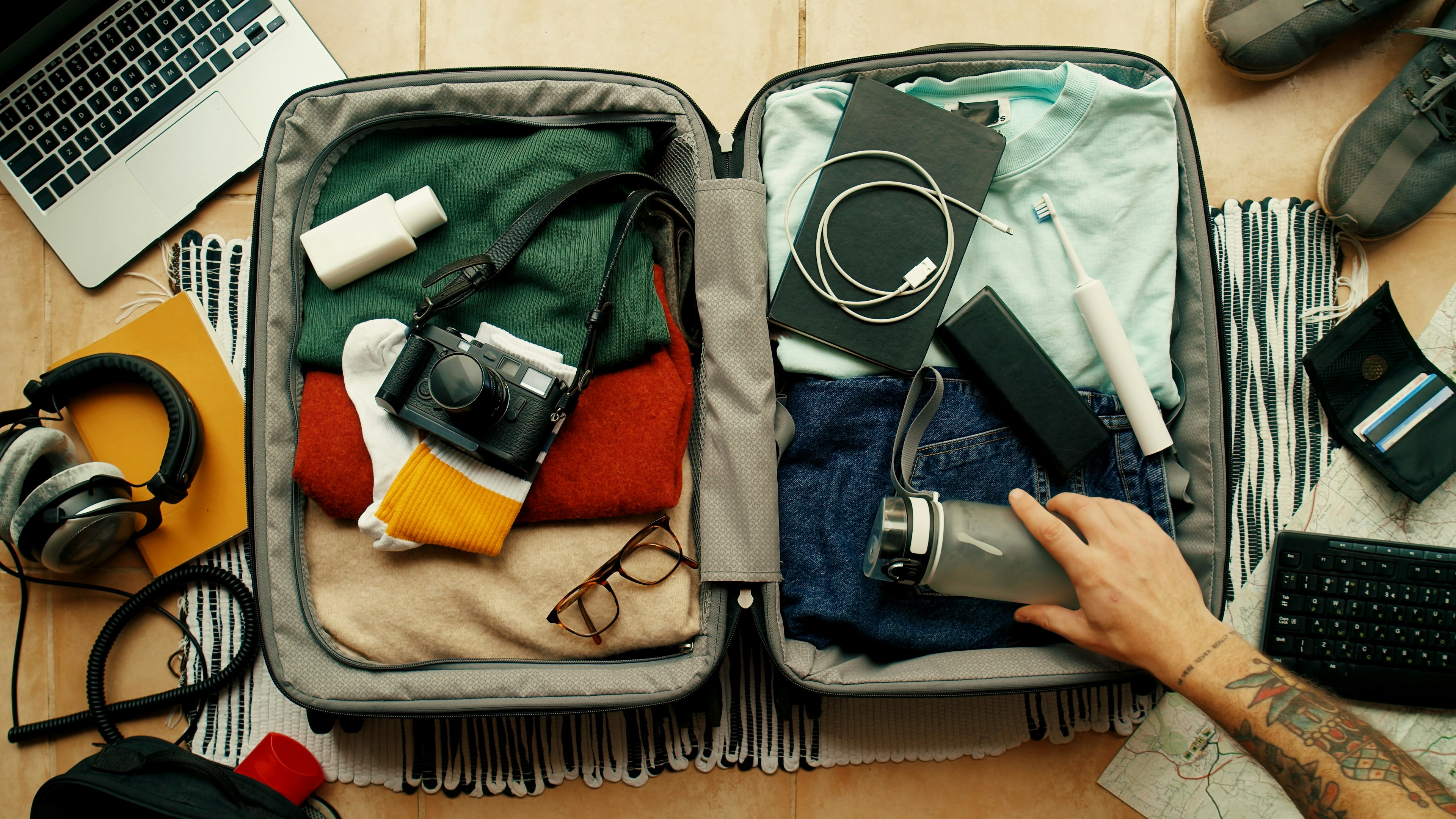 Man with tatted arm packs suitcase for adventure travel trip.