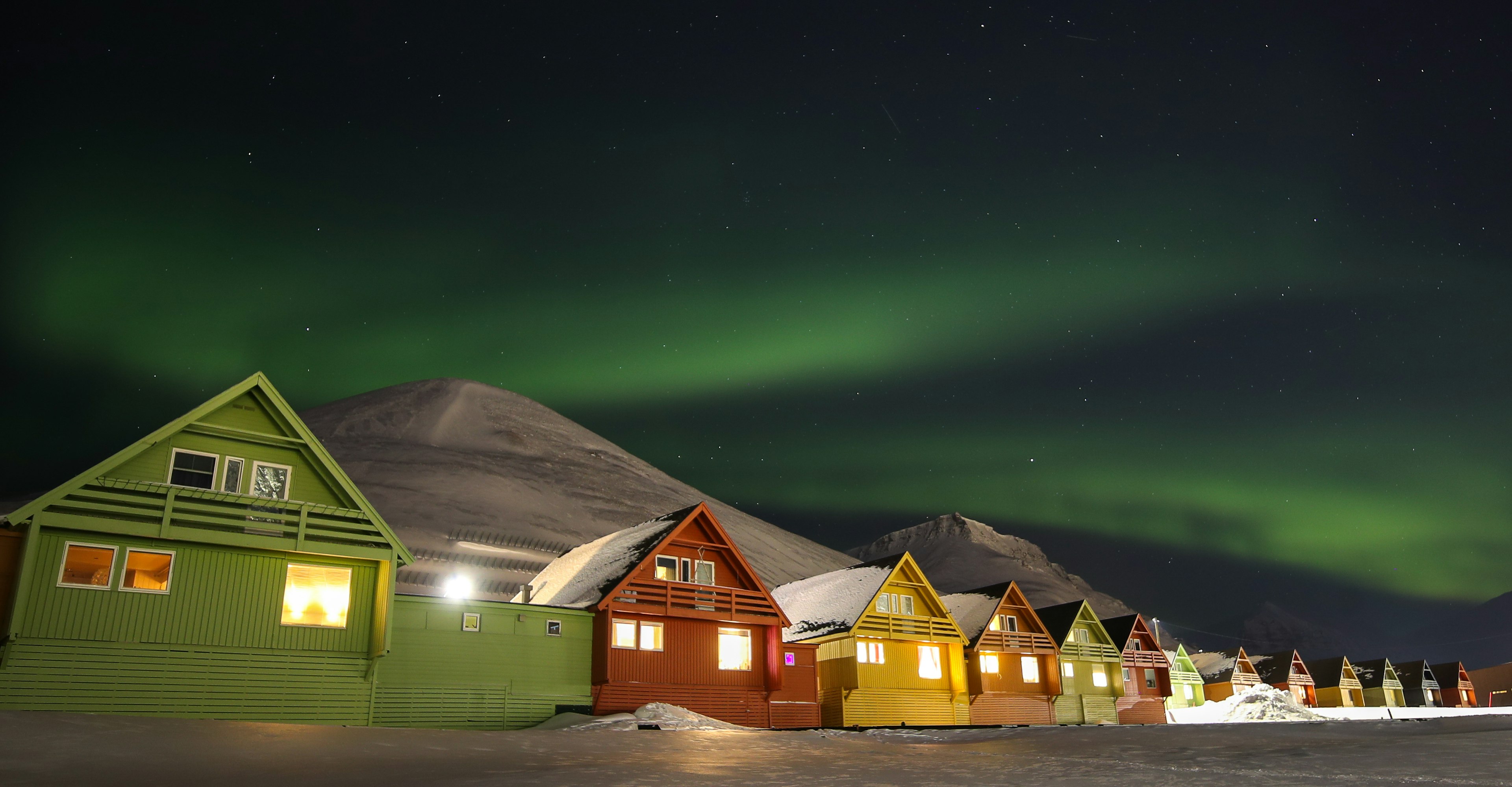 A row of colorful houses in Longyearbyen with a mountain in the background under the northern lights.