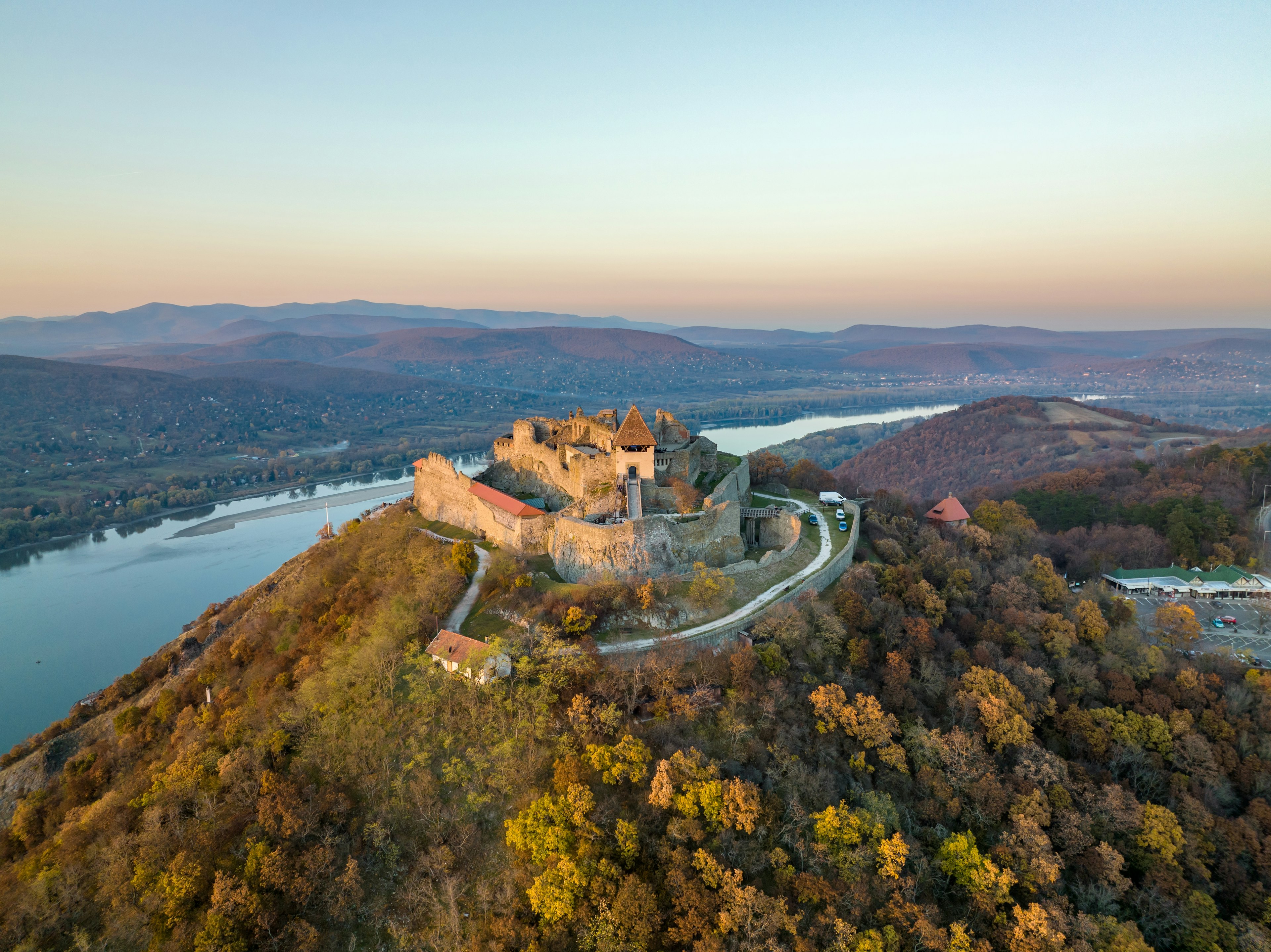 Aerial panoramic drone view of the beautiful high castle of Visegrad on a moody autumn sunset along the Danube Bend (Dunakanyar) and amazing golden sunset at background.