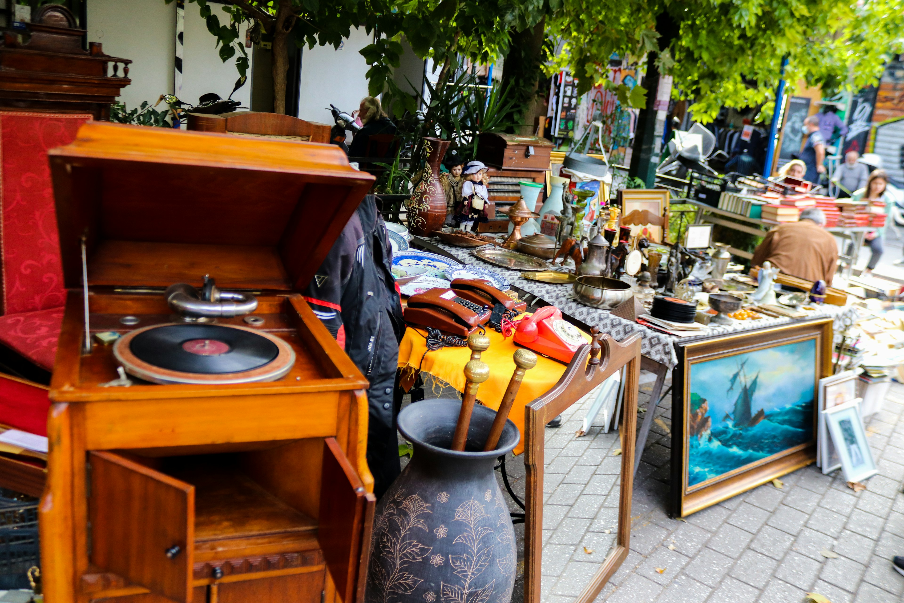 Vases, a record player, paintings, and general bric-a-brac on display on a pavement at a flea market