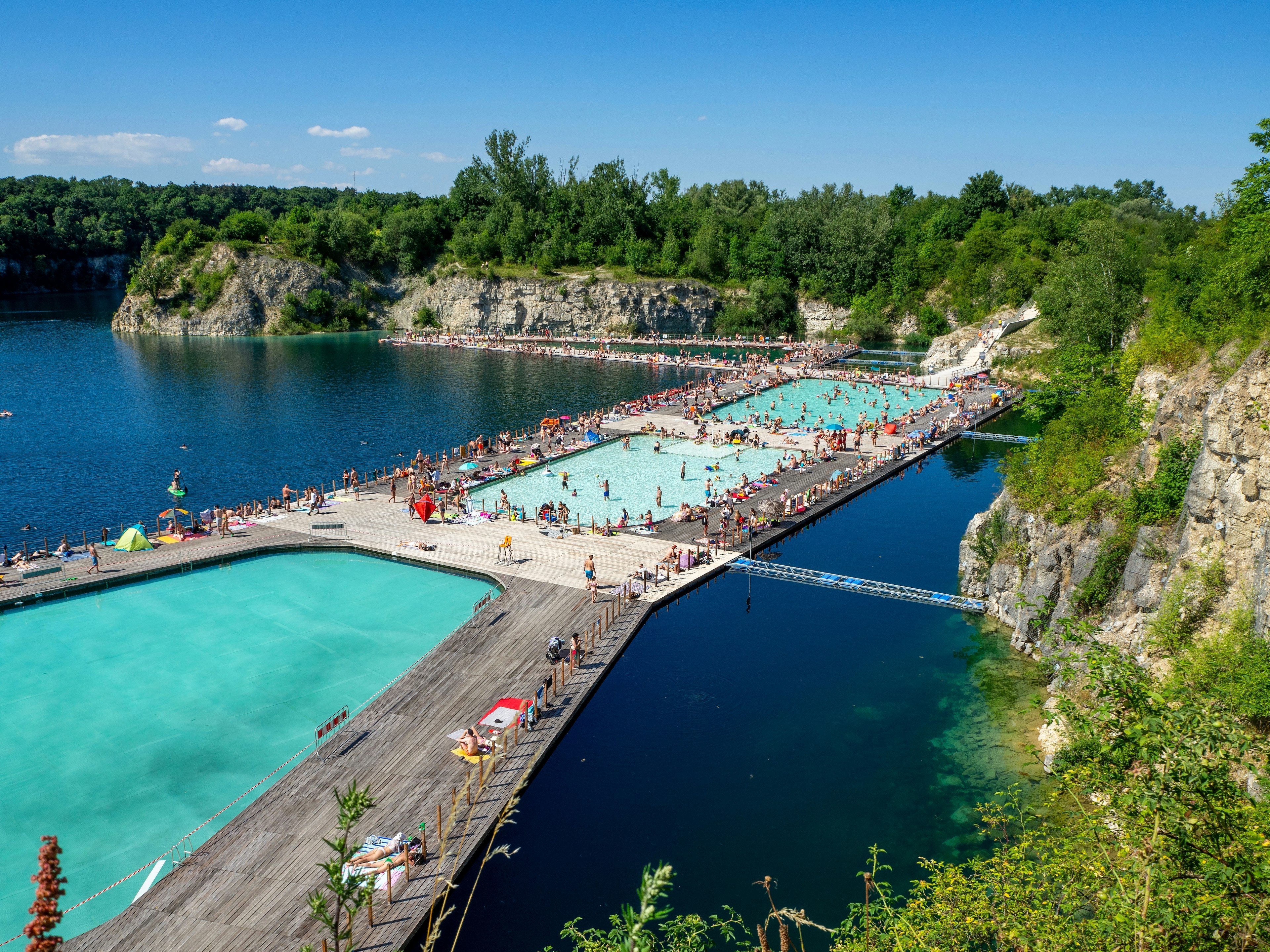 An aerial view of people enjoying floating pools and connected decks at Zakrzowek, a former quarry turned swimming spot in Kraków, Poland