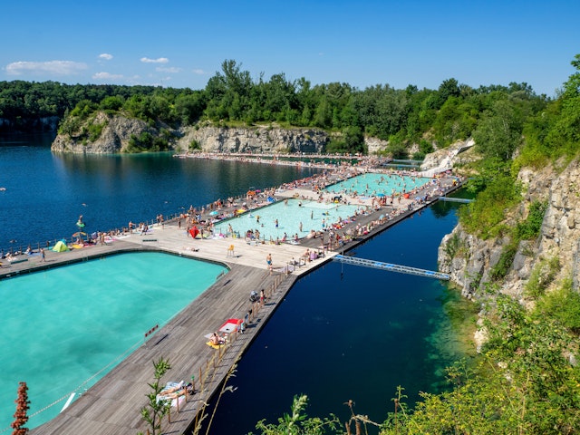 An aerial view of people enjoying floating pools and connected decks at Zakrzowek, a former quarry turned swimming spot in Kraków, Poland
