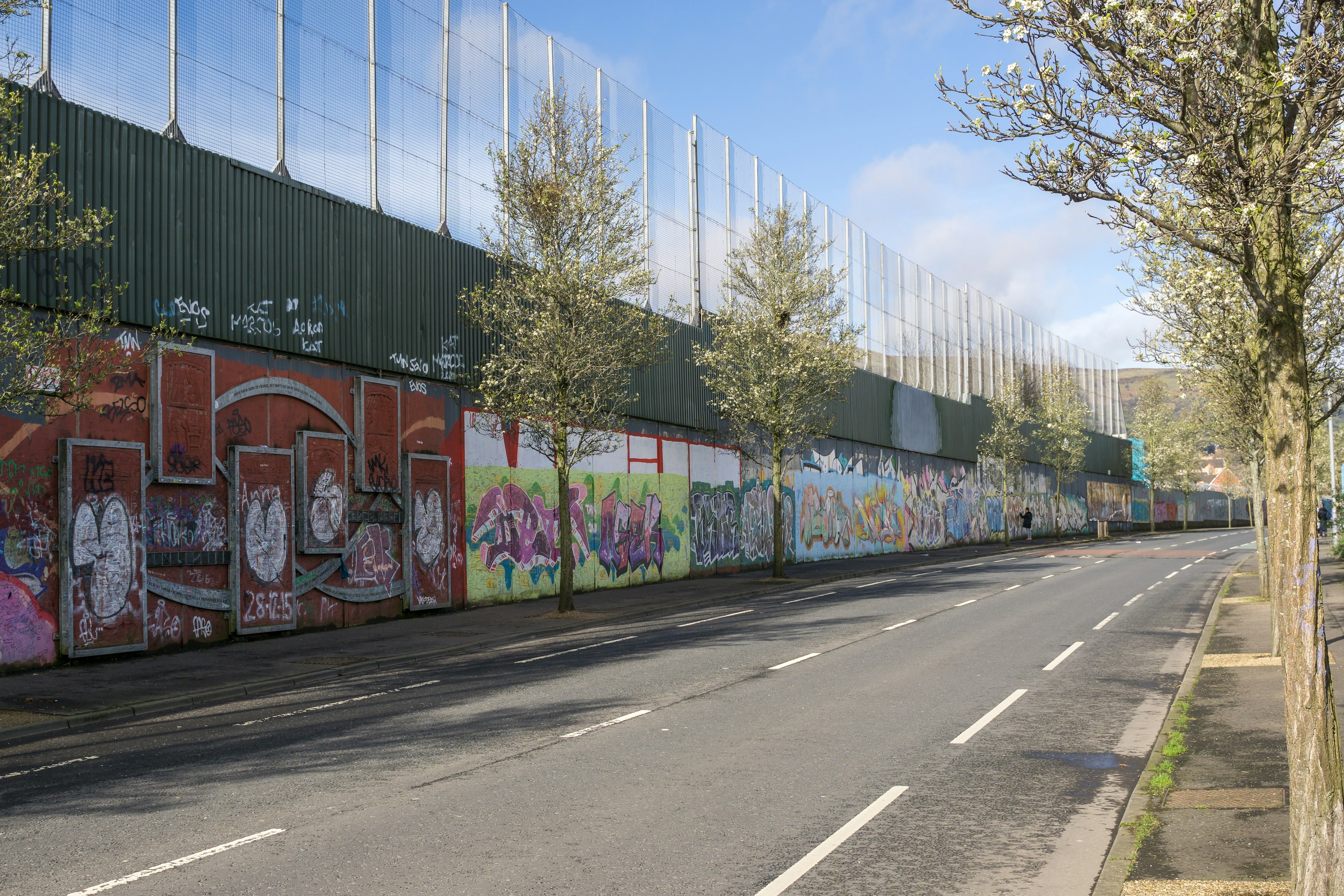 The tall brick wall topped with a sheet metal partition that forms the 'peace line' in this part of Belfast.