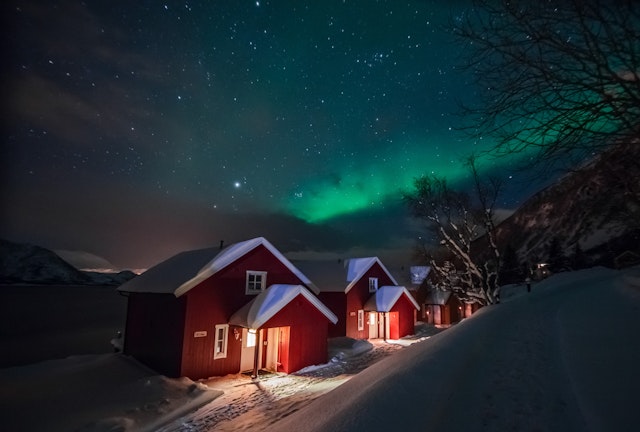 Northern lights (Aurora Borealis) over the red snowed-in cottages in a Lapland village.
