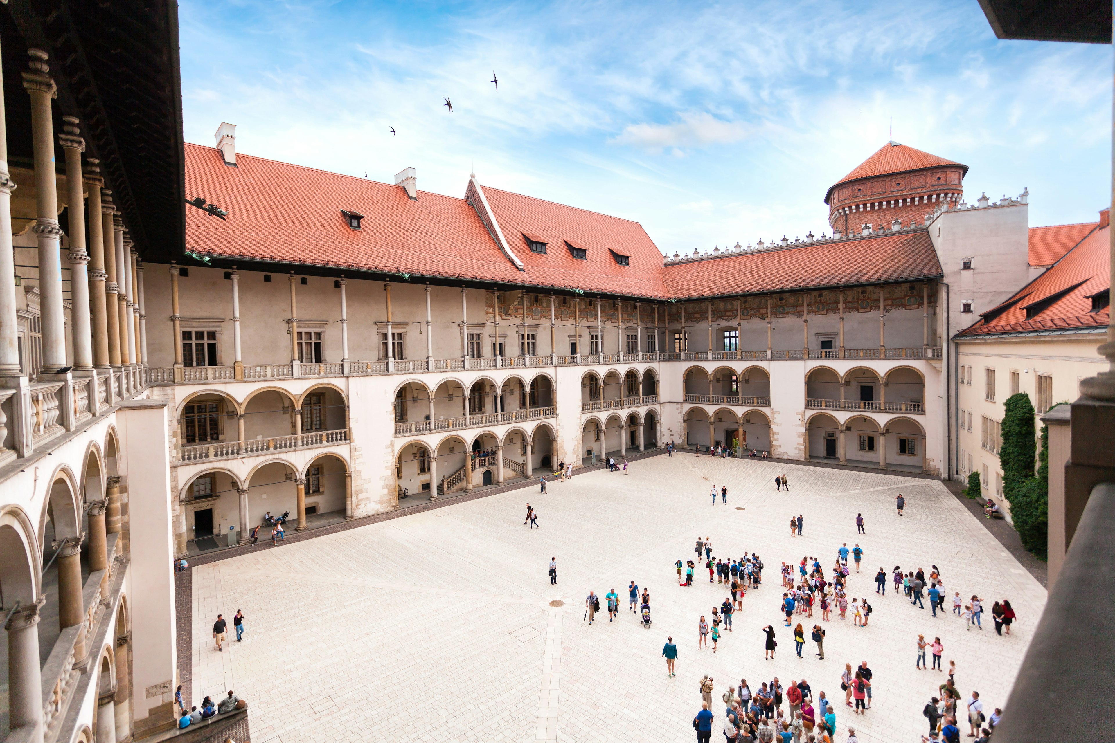 A wide shot of people gathering in the courtyard of a Renaissance-style palace, surrounded by balconies, walkways and loges