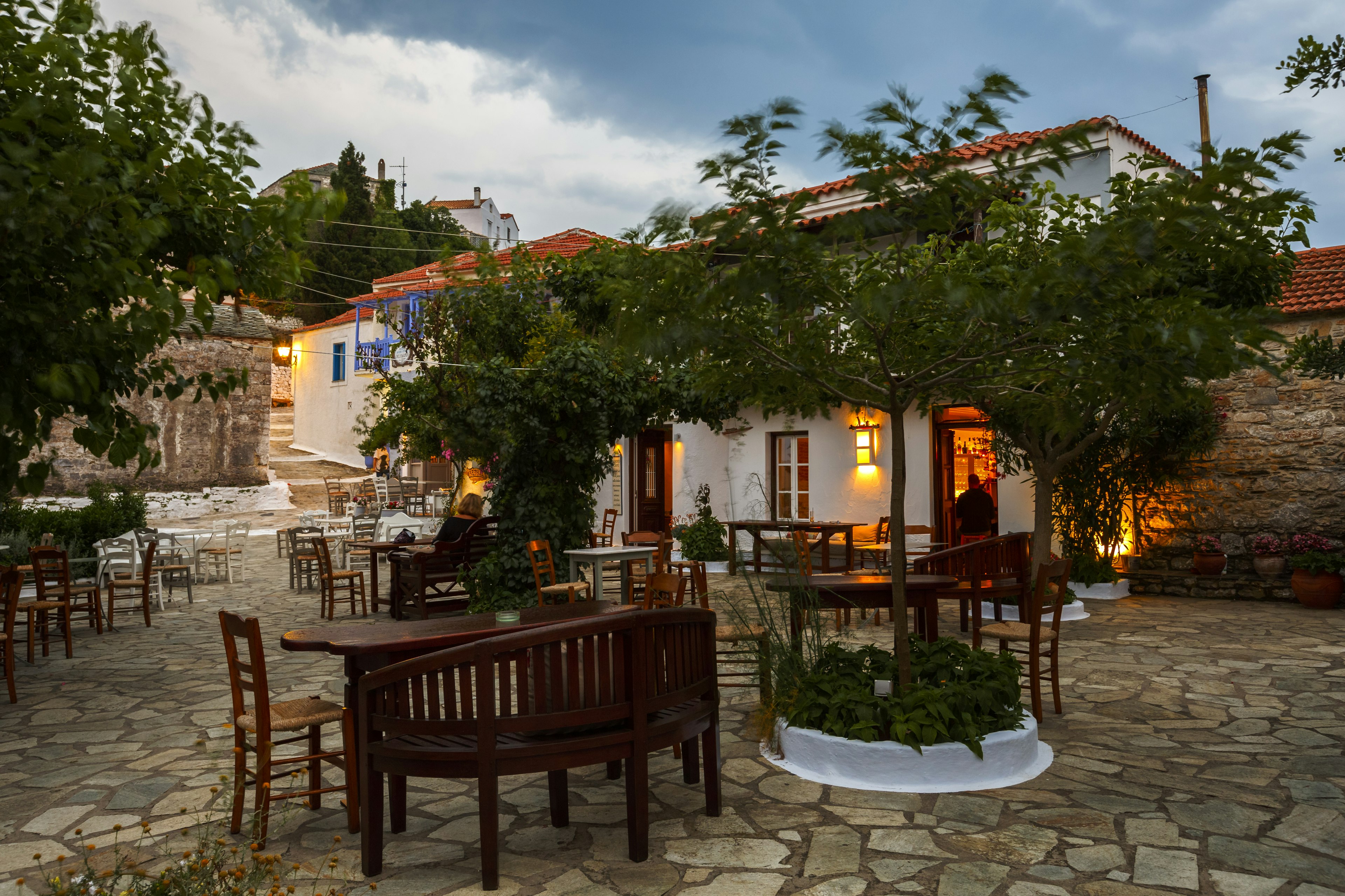 Empty tables outside a restaurant in a cobbled square in Chora of Alonissos island, Greece.