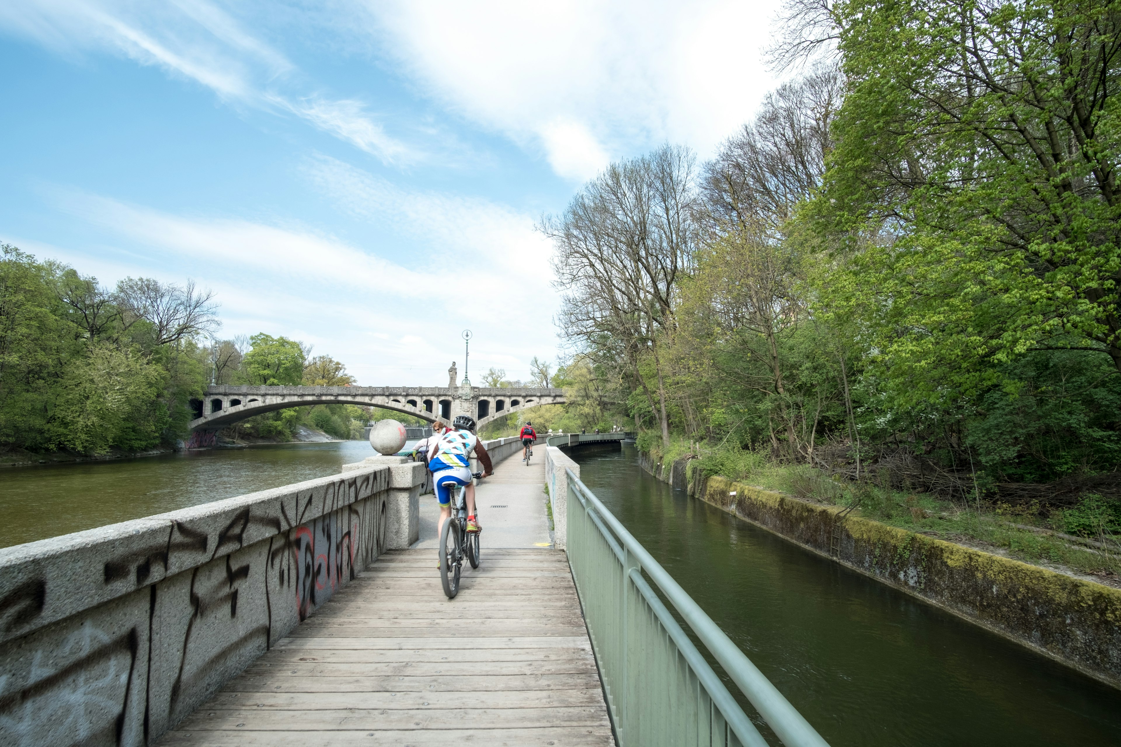 Two people cycle along a wooden path on the river bank of Isar river in Munich.