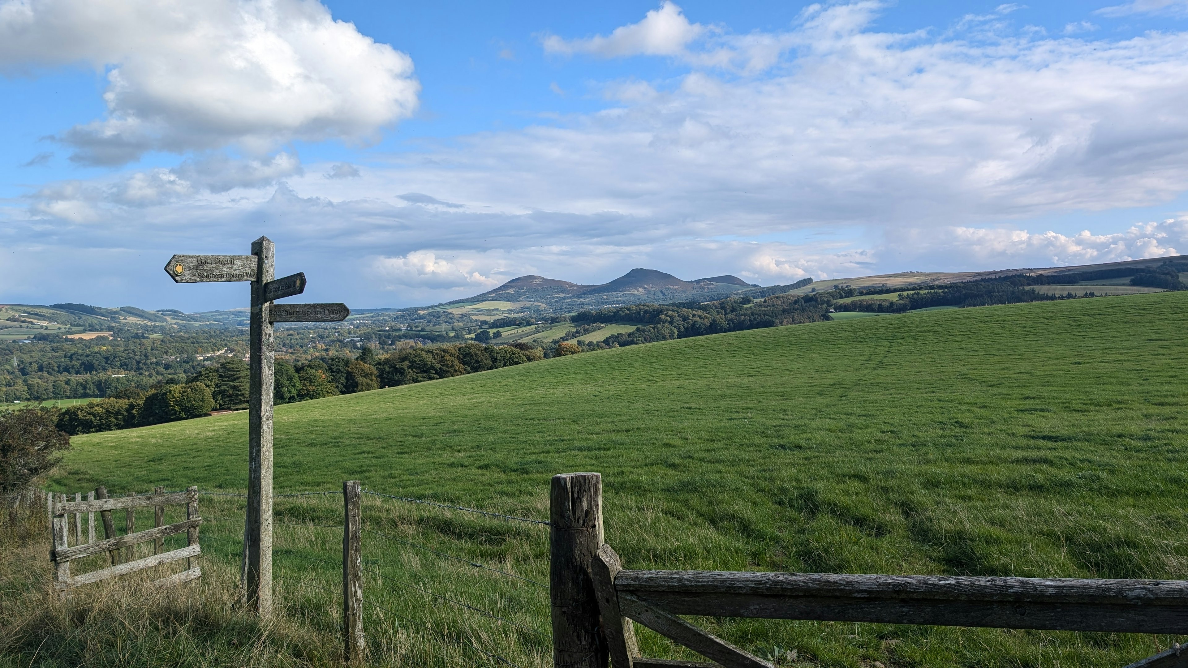 Views over green fields and hills on a hiking trail with a signpost pointing out the different routes